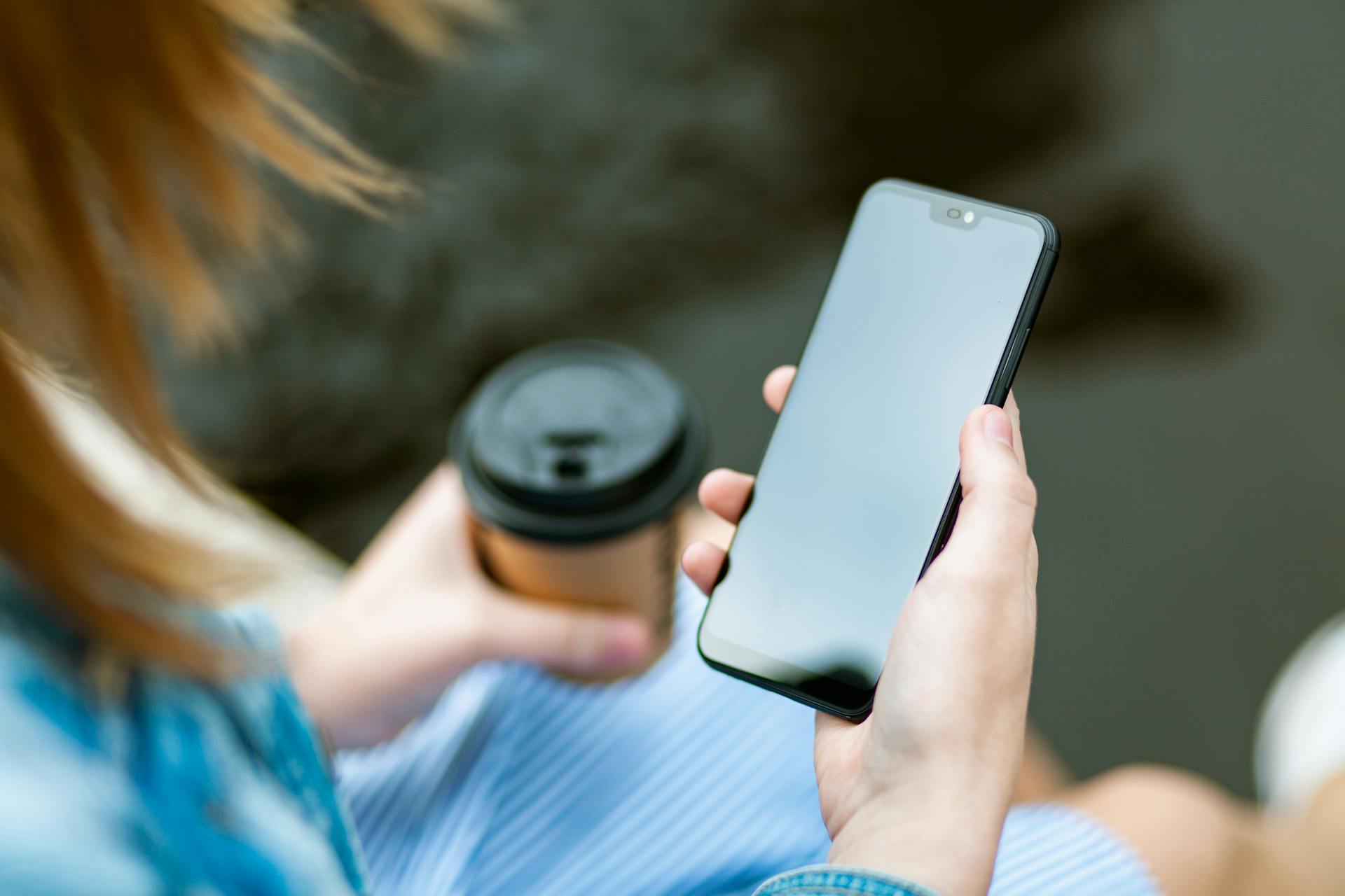 A woman holding her phone and a coffee cup | Source: Pexels