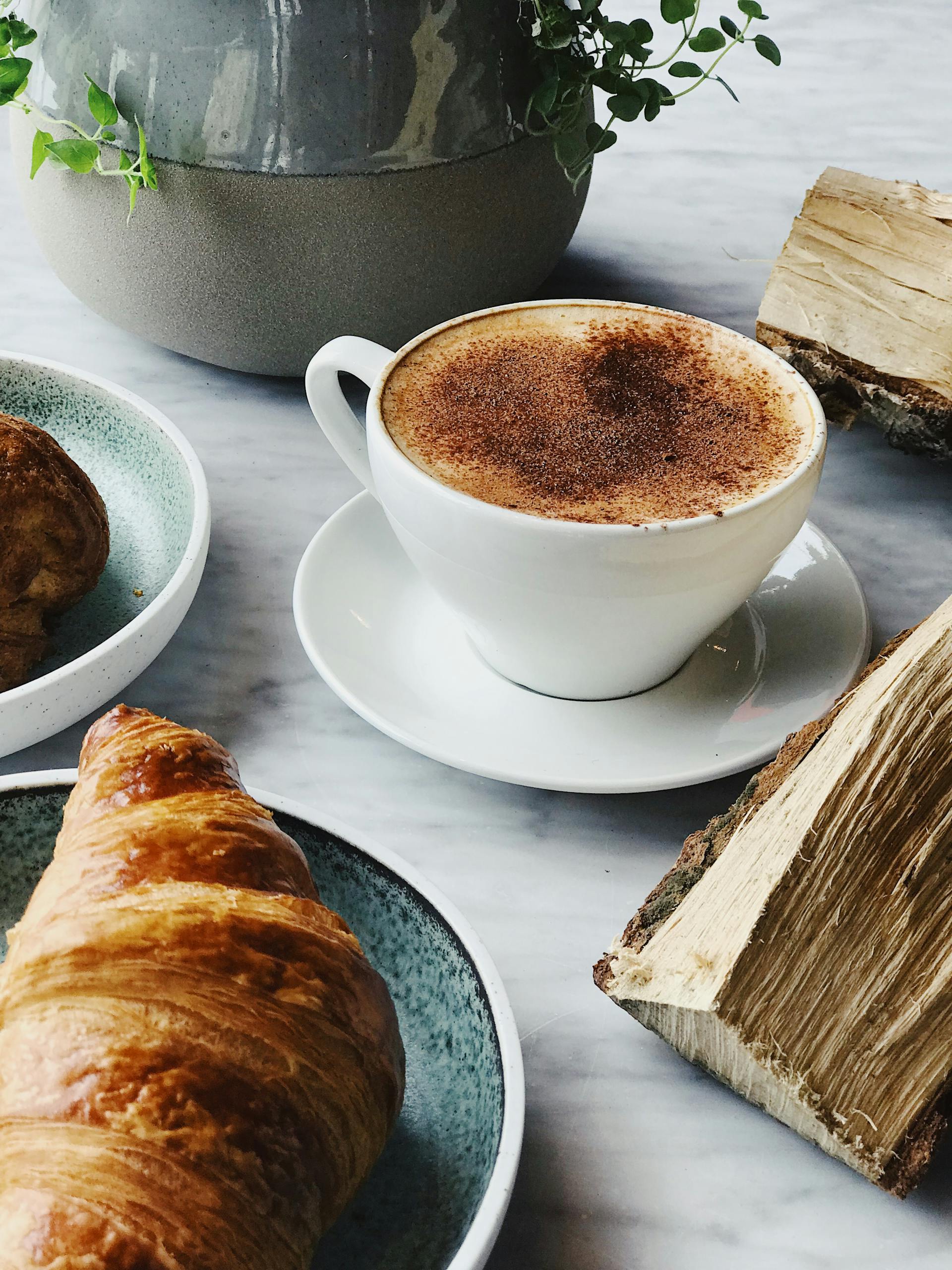A cup of coffee and a croissant lying on a table | Source: Pexels