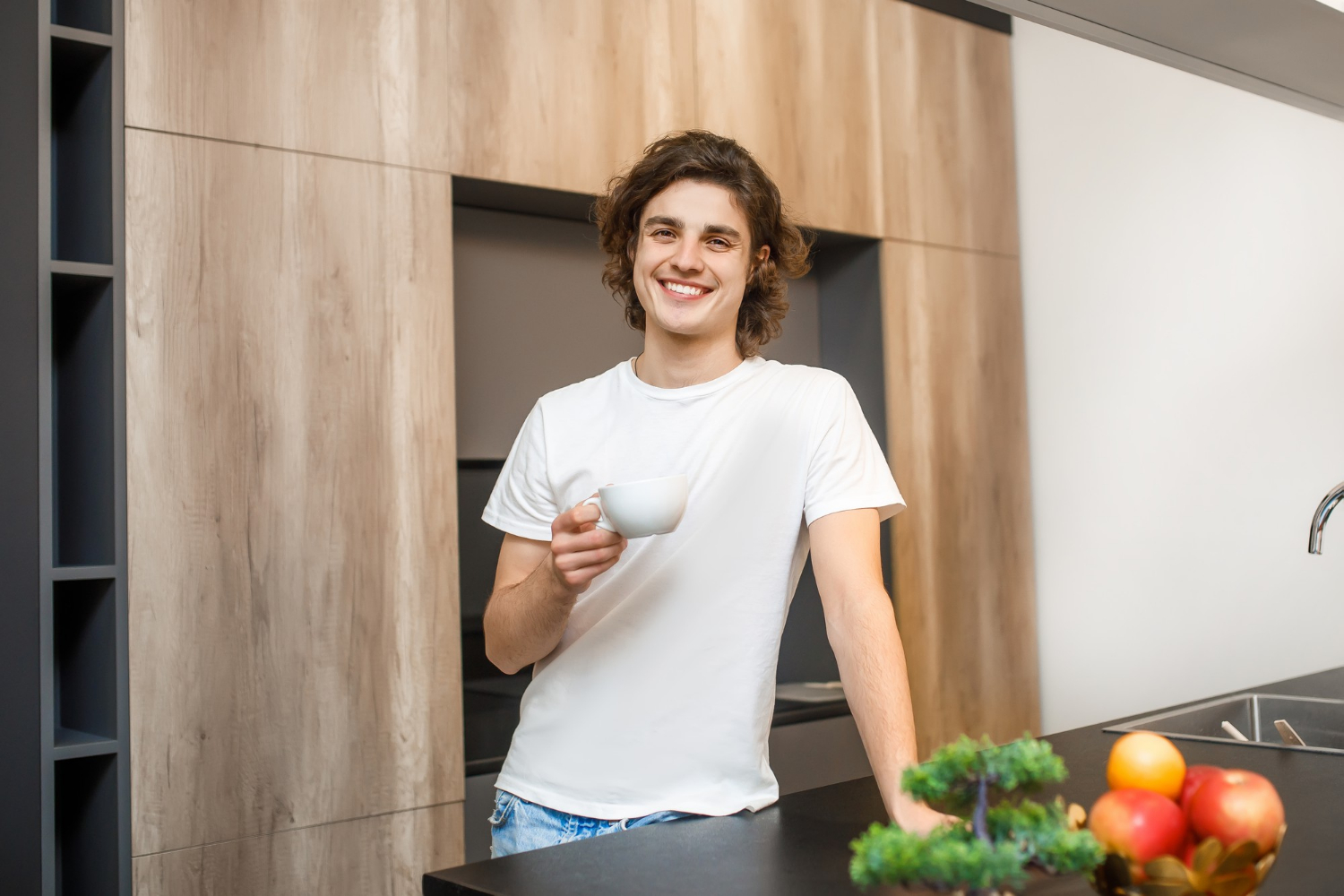 A smiling man holding a white ceramic cup and standing in the kitchen | Source: Freepik