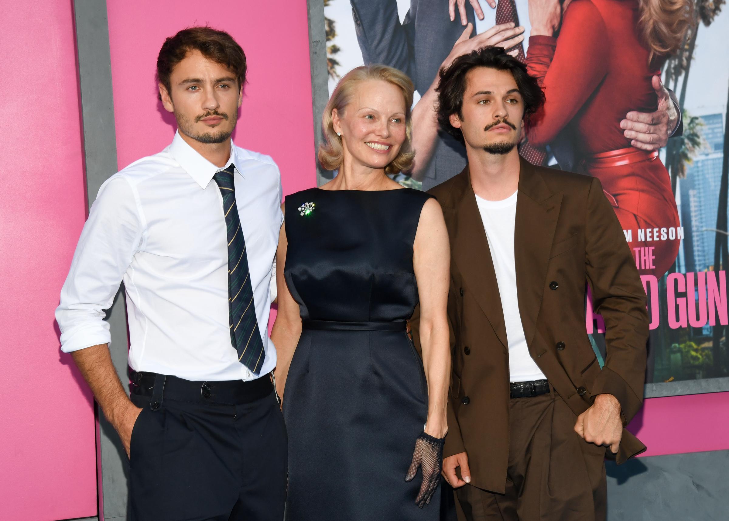 Pamela Anderson poses with her sons Brandon Thomas Lee and Dylan Jagger Lee at the premiere of The Last Showgirl in Los Angeles, California. Pamela wore a sleek dark dress with sheer gloves, while Brandon and Dylan stood beside her in smart casual looks. | Source: Getty Images