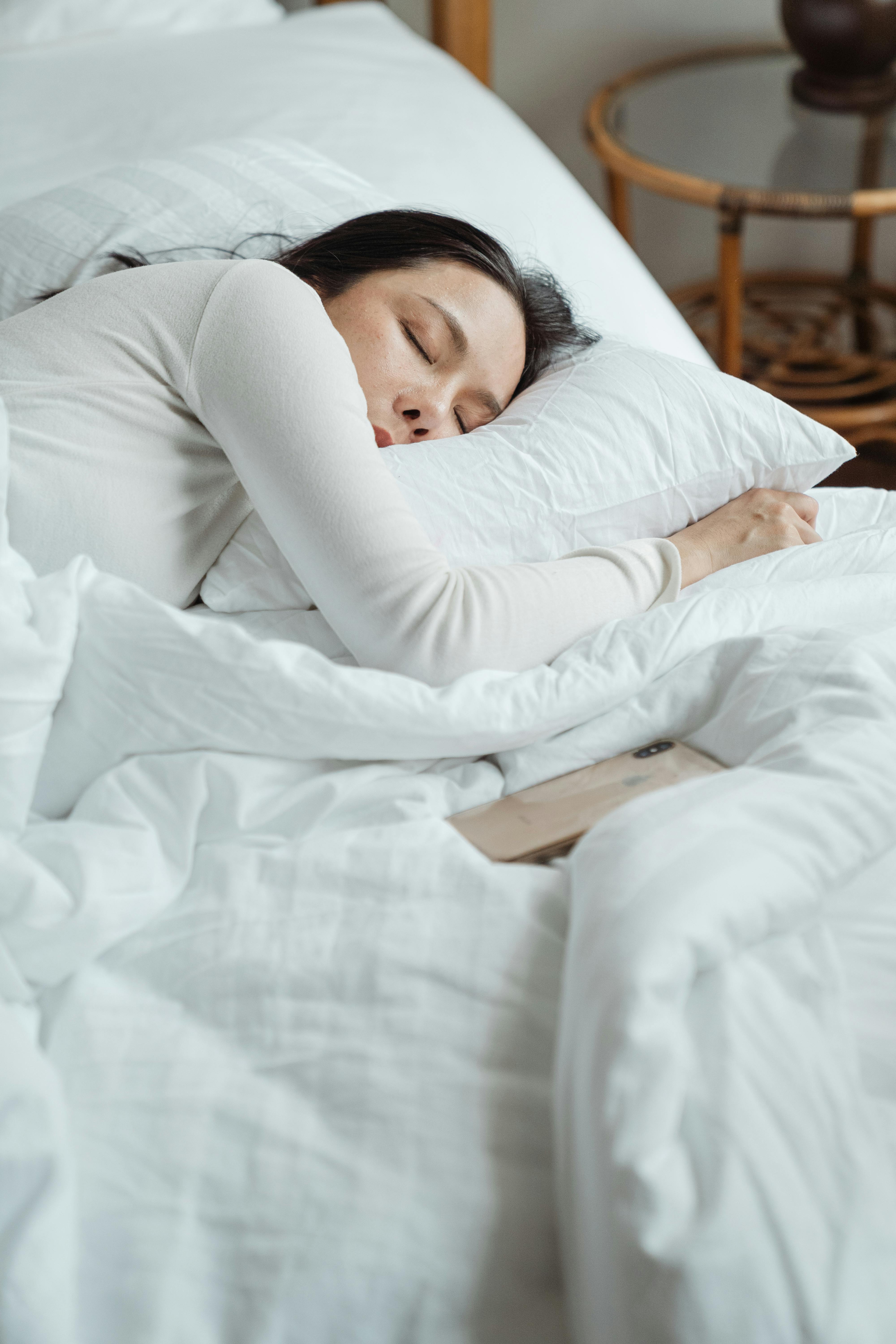 A woman lying in bed alone with her phone on the side | Source: Pexels