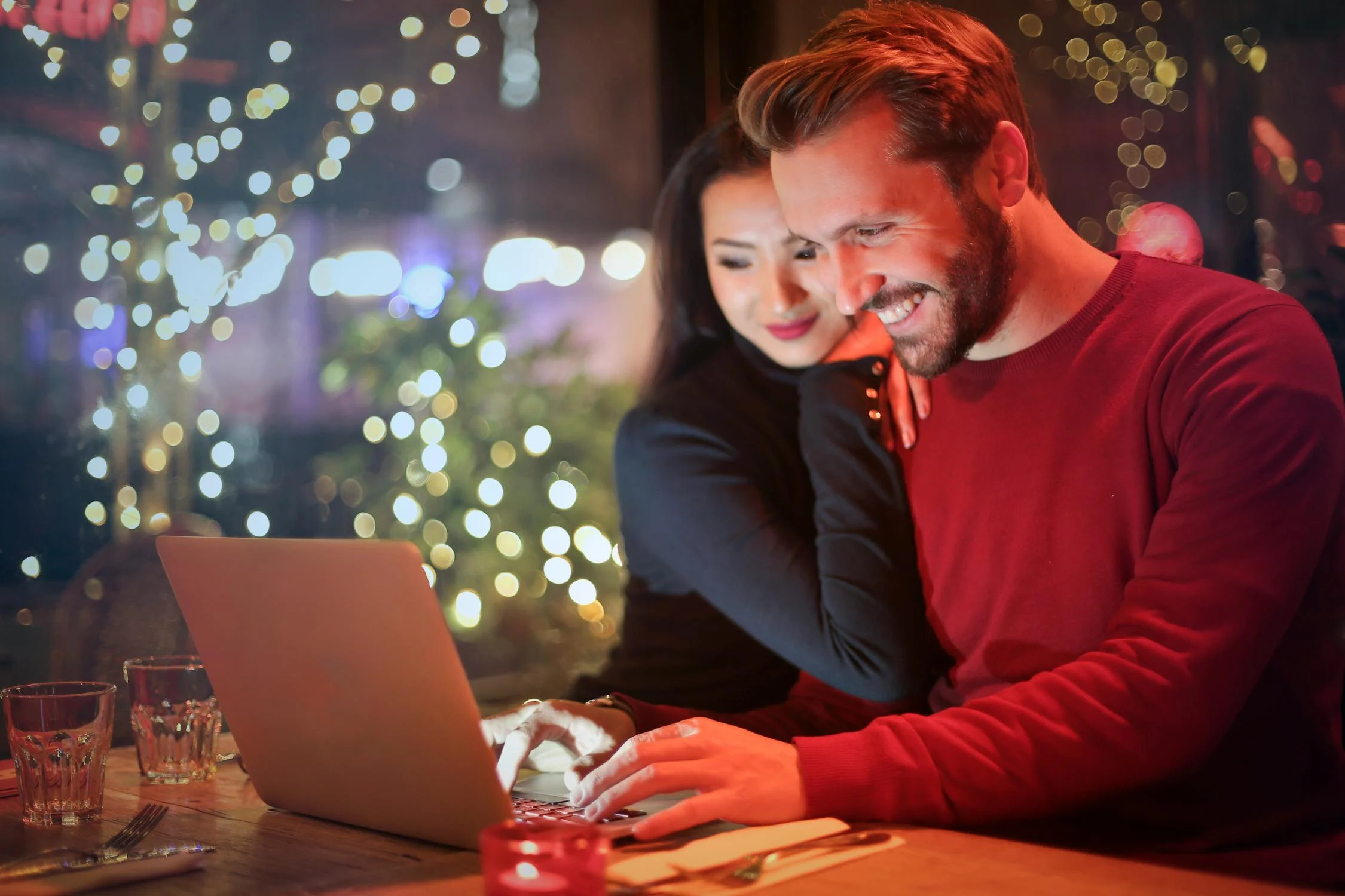 A woman leaning against a man who's smiling while working on his laptop | Source: Pexels