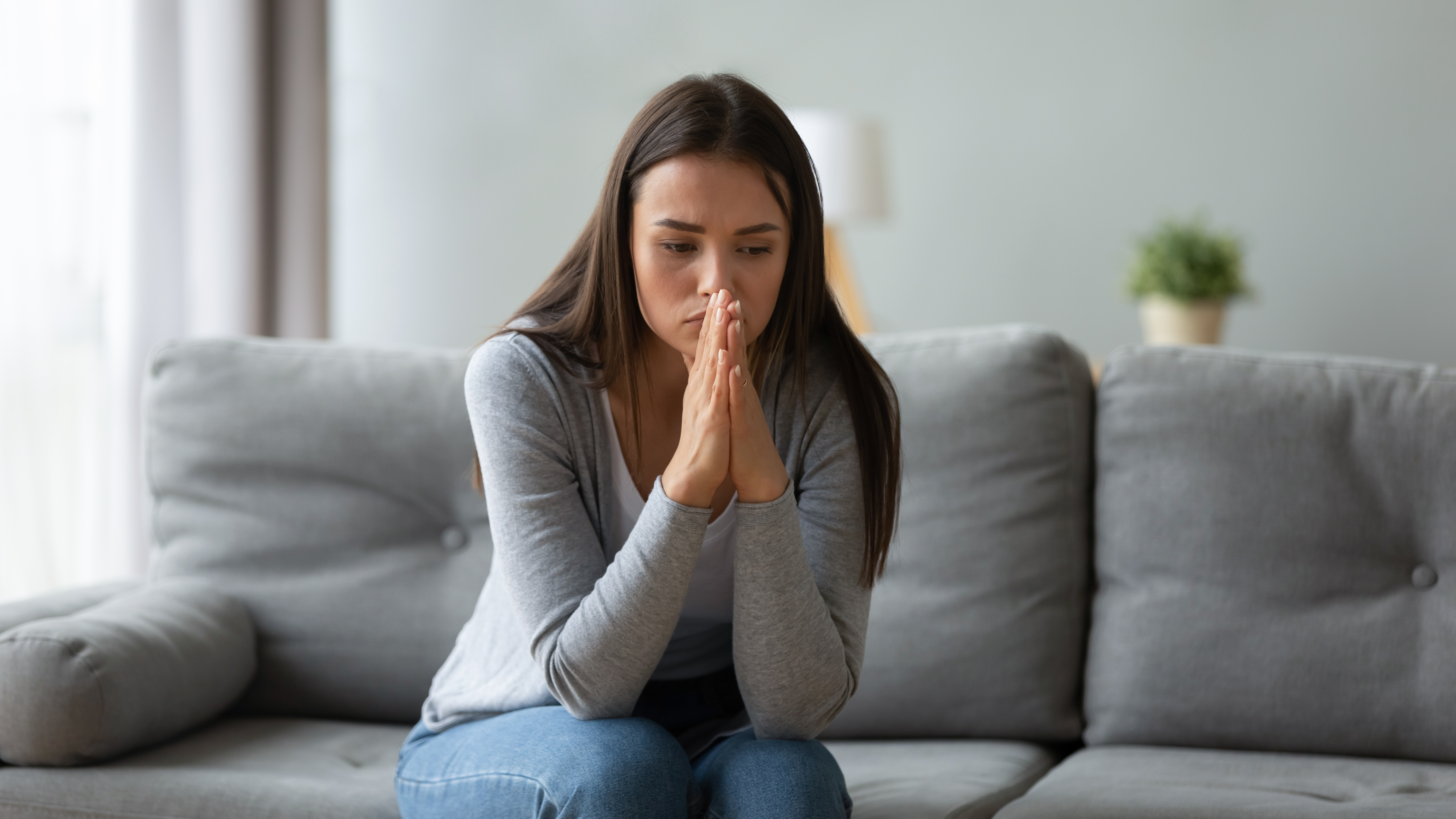 A distressed woman sitting alone on a sofa | Source: Shutterstock