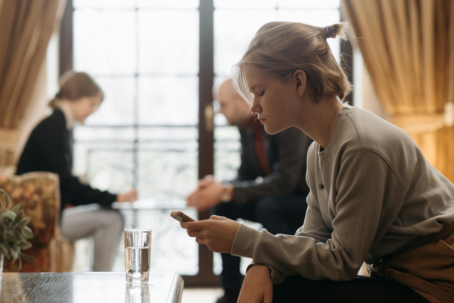 A serious girl looking at her phone while other people appear in the background | Source: Pexels