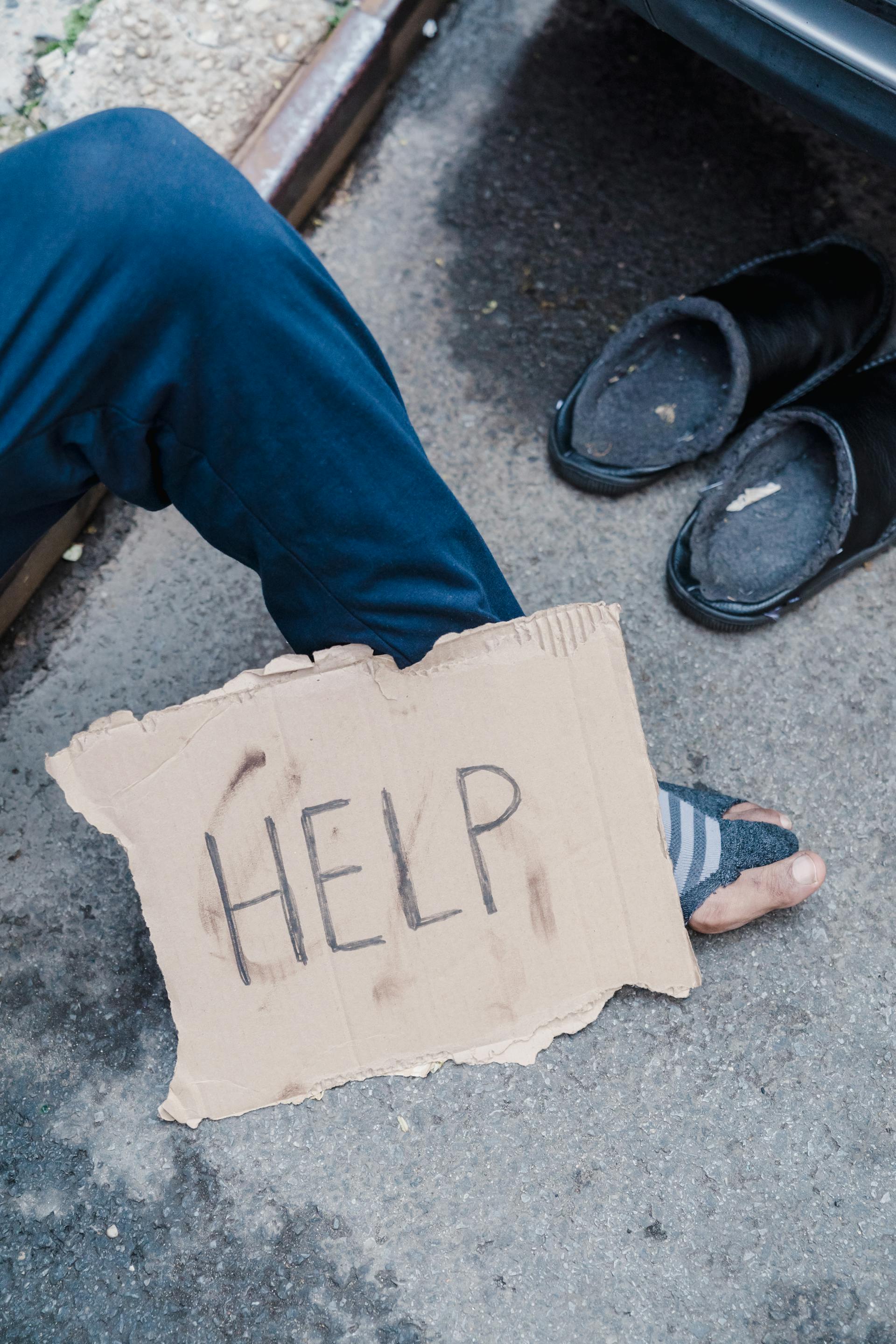A cardboard sign lying next to a homeless man | Source: Pexels