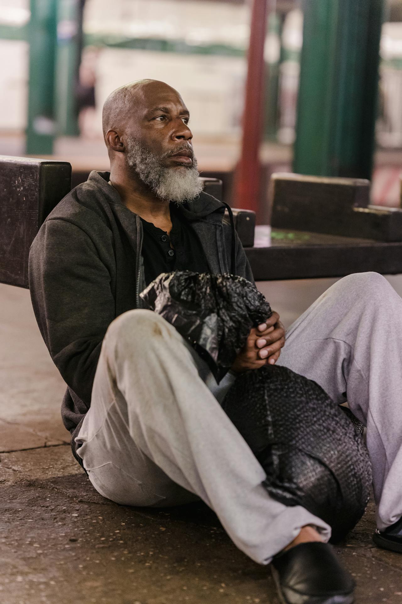 An older man sitting on a concrete floor while holding a garbage bag | Source: Pexels