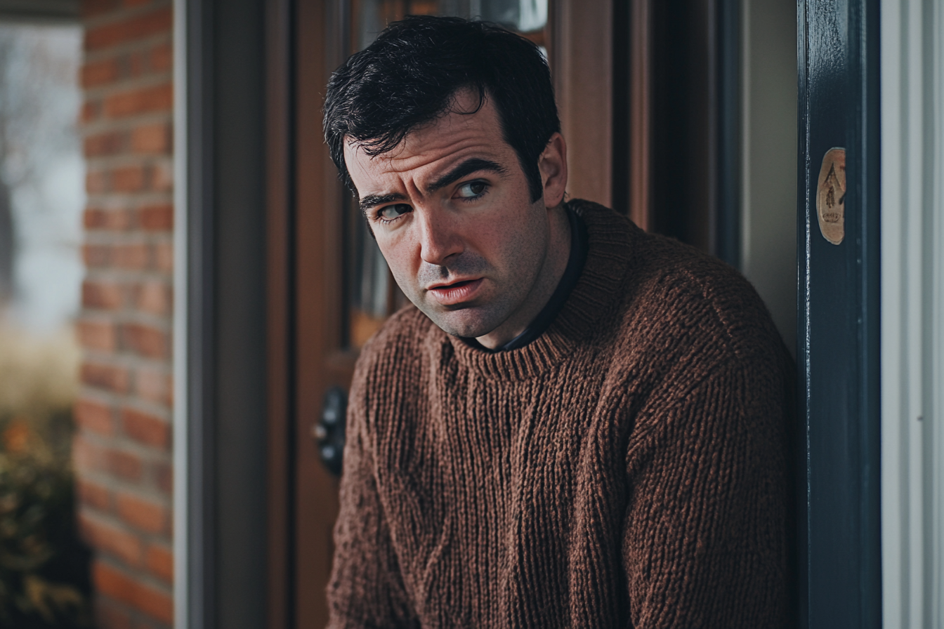 A remorseful man standing near a front door | Source: Midjourney