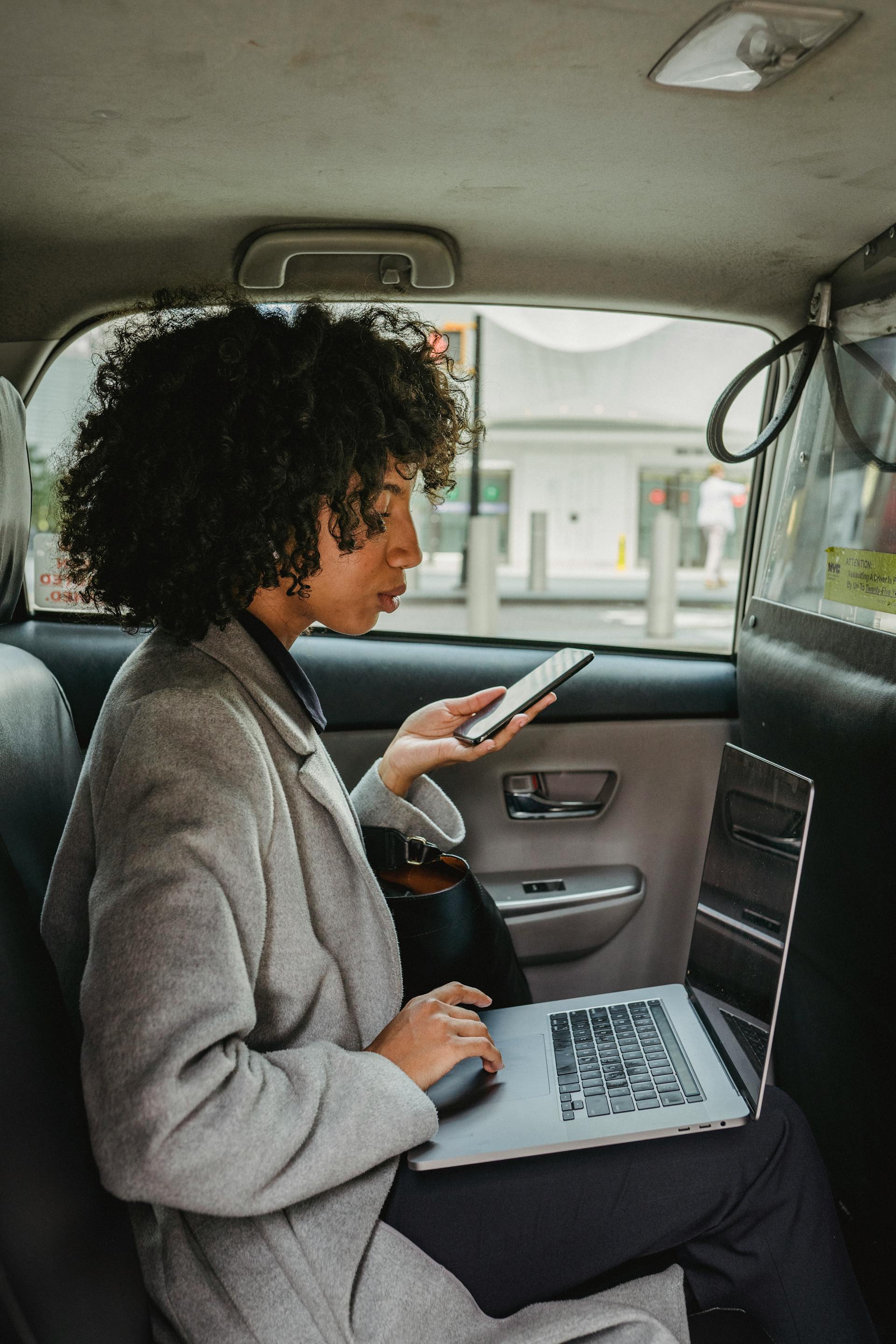 A serious woman holding a phone and using a laptop | Source: Pexels
