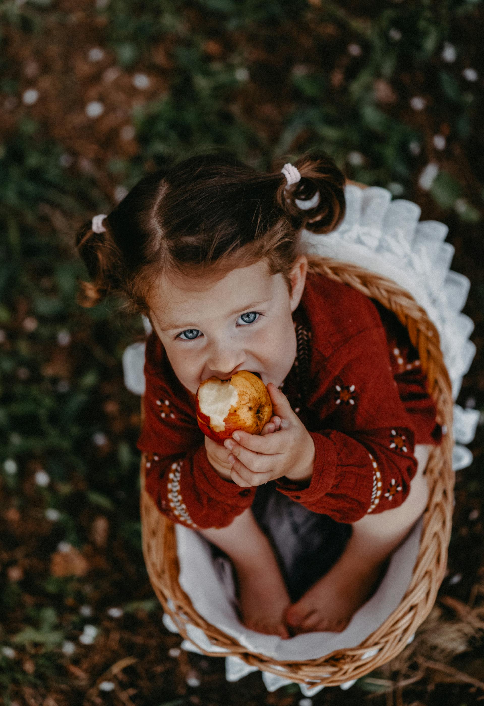 A girl sitting in a basket eating an apple | Source: Pexels