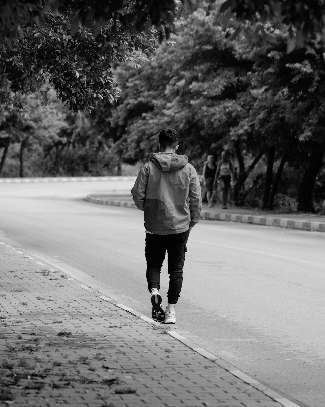 Grayscale shot of a young man walking on the road | Source: Pexels