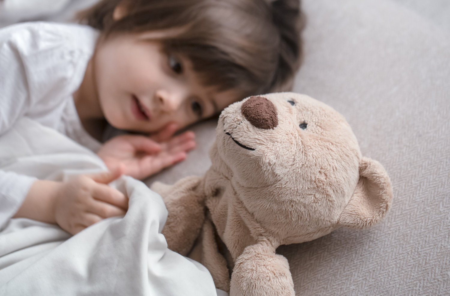 A little girl lying in her bed beside her stuffed teddy bear | Source: Freepik