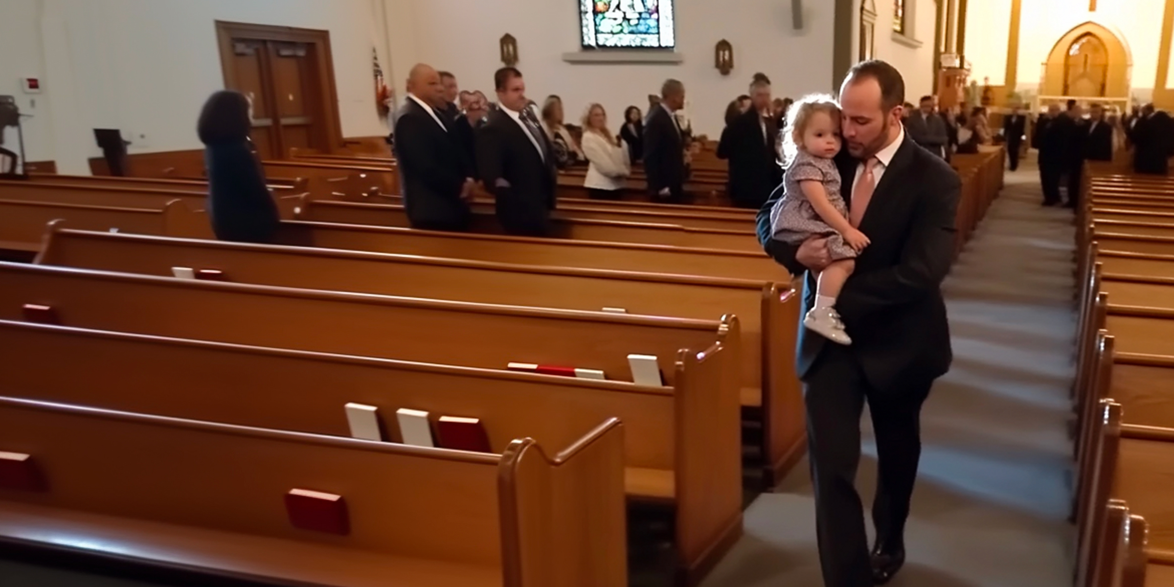 A man walking down a church aisle with a little girl in his arms | Source: Amomama