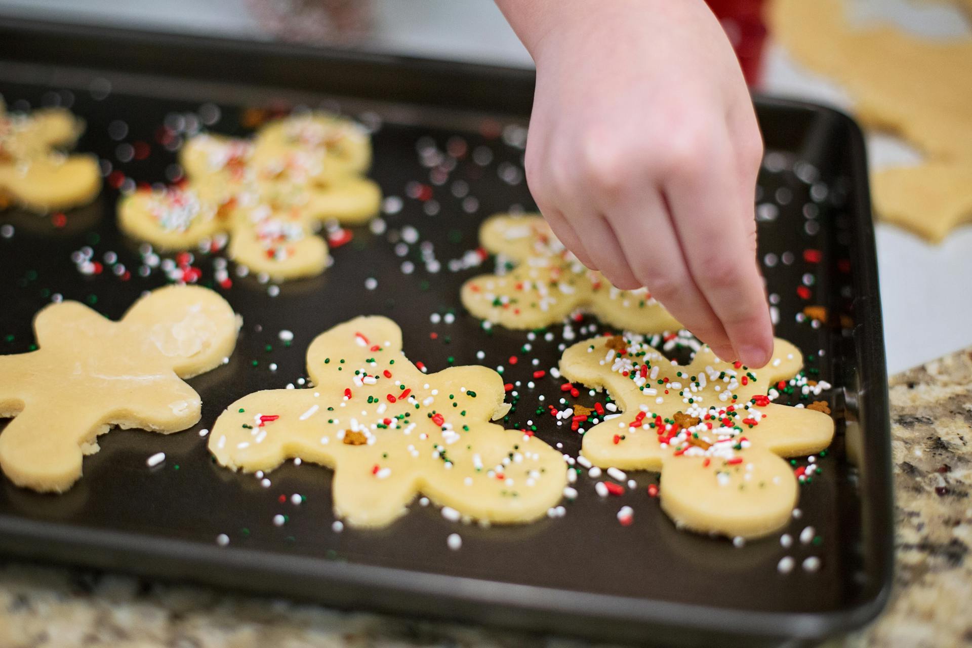 A girl pouring sprinkles on gingerbread cookies | Source: Pexels