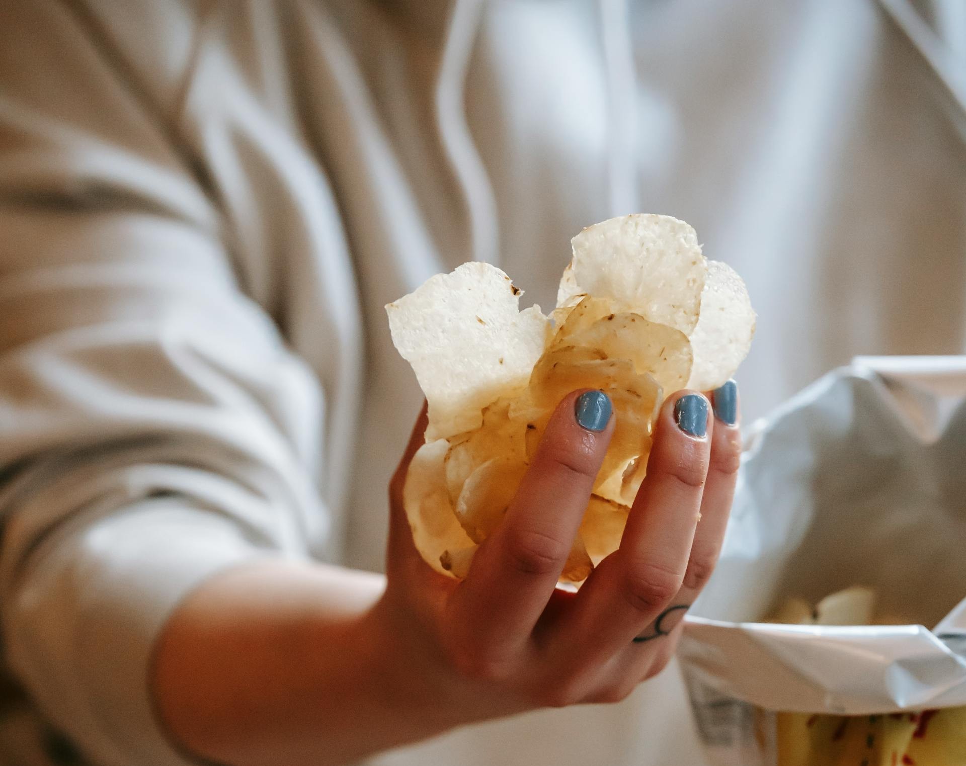 A woman holding a handful of potato chips | Source: Pexels