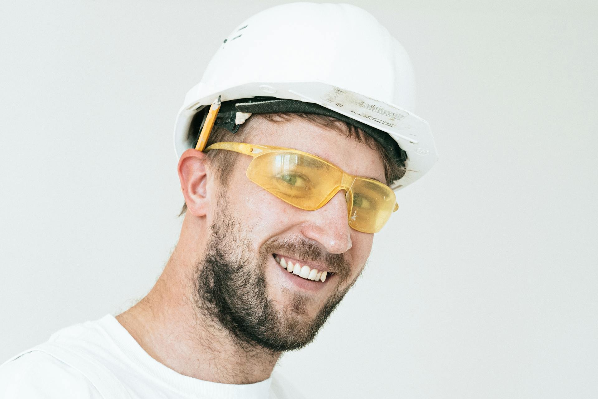 A smiling construction worker wearing a white hard hat and yellow safety glasses | Source: Pexels