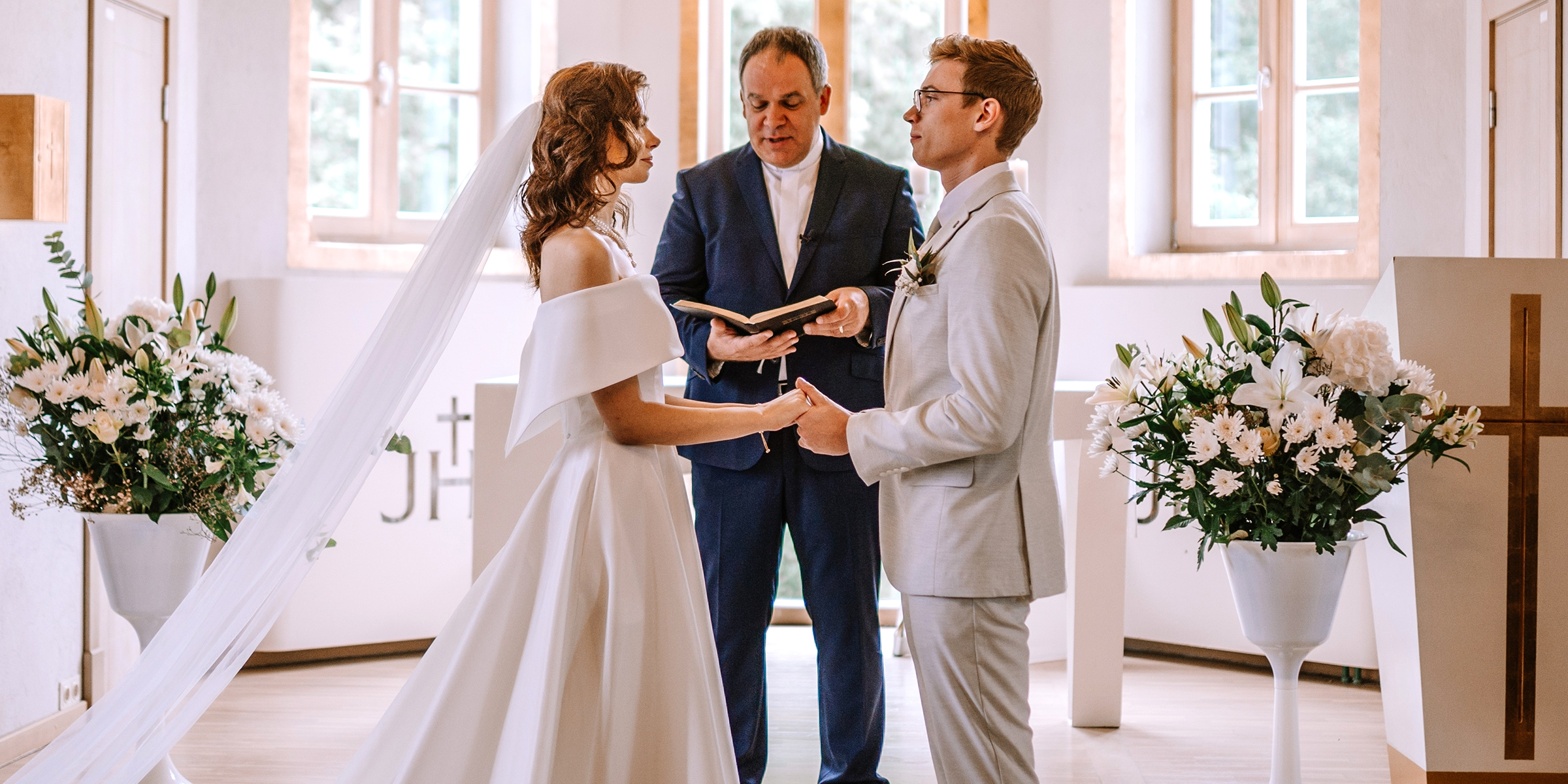 A bride and groom standing at the altar holding hands as a priest reads their vows | Source: Shutterstock