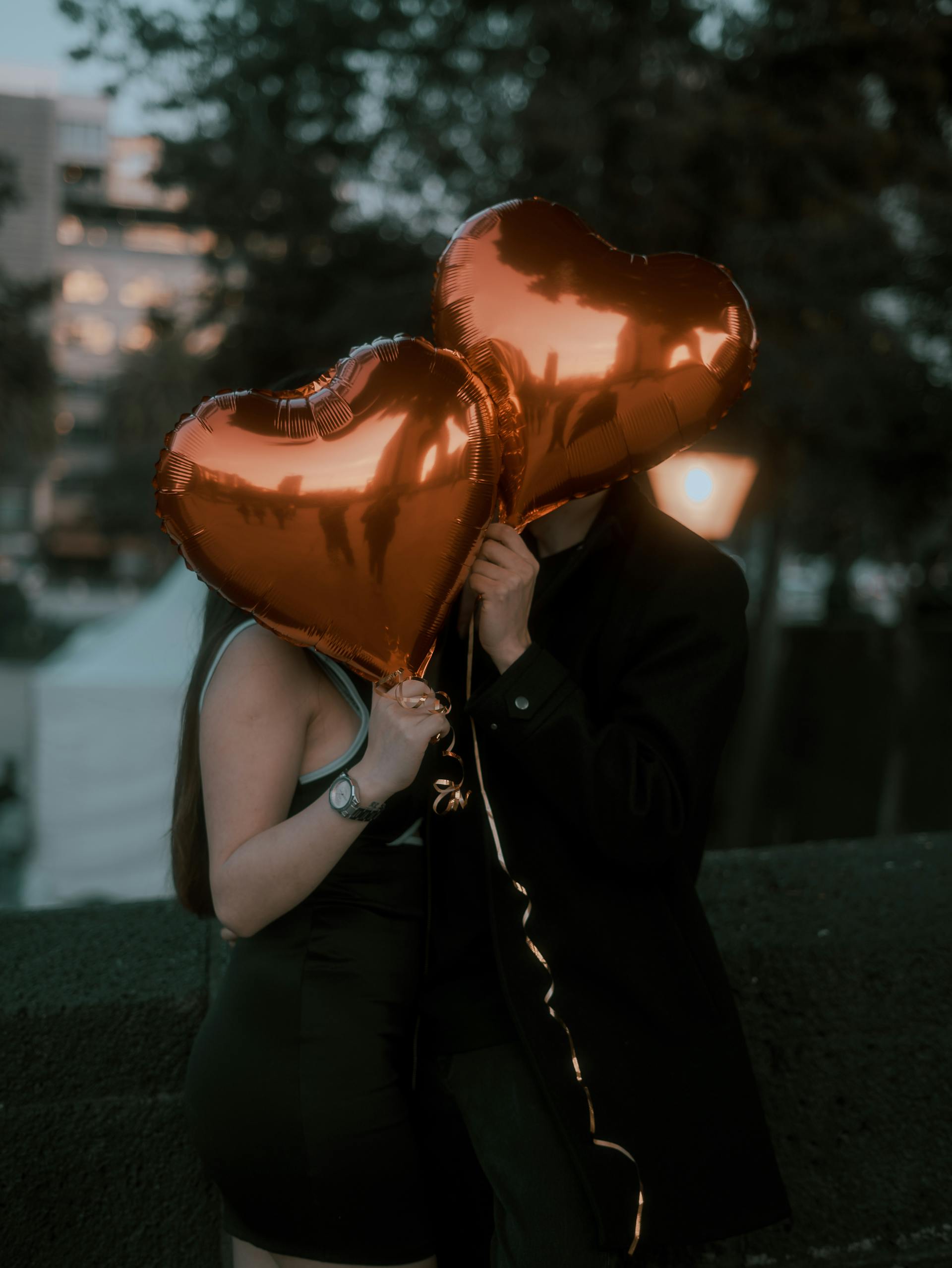 A couple hiding their faces with heart-shaped balloons | Source: Pexels