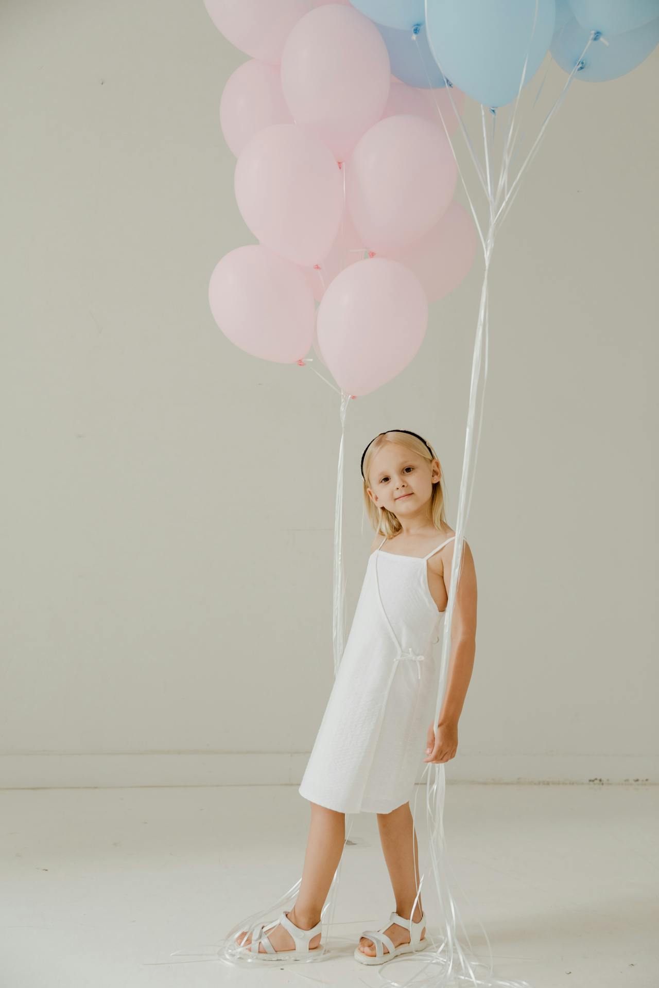An excited little girl holding pink and blue balloons | Source: Pexels
