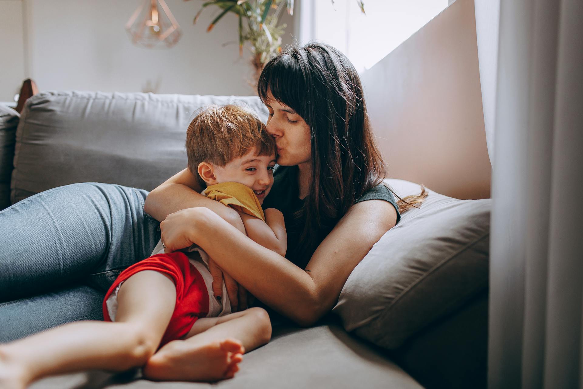 A woman kissing and hugging her son while sitting on a couch | Source: Pexels