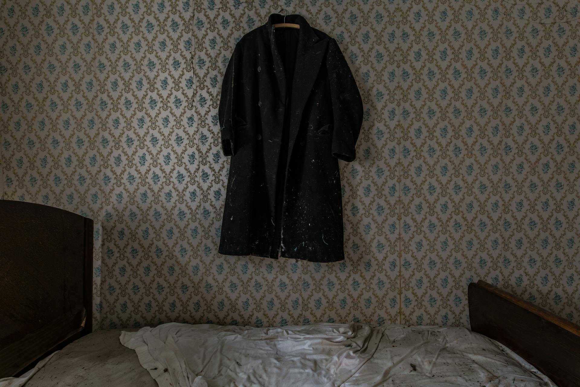An old-looking mattress in a room with a hanging jacket on the wall | Source: Pexels