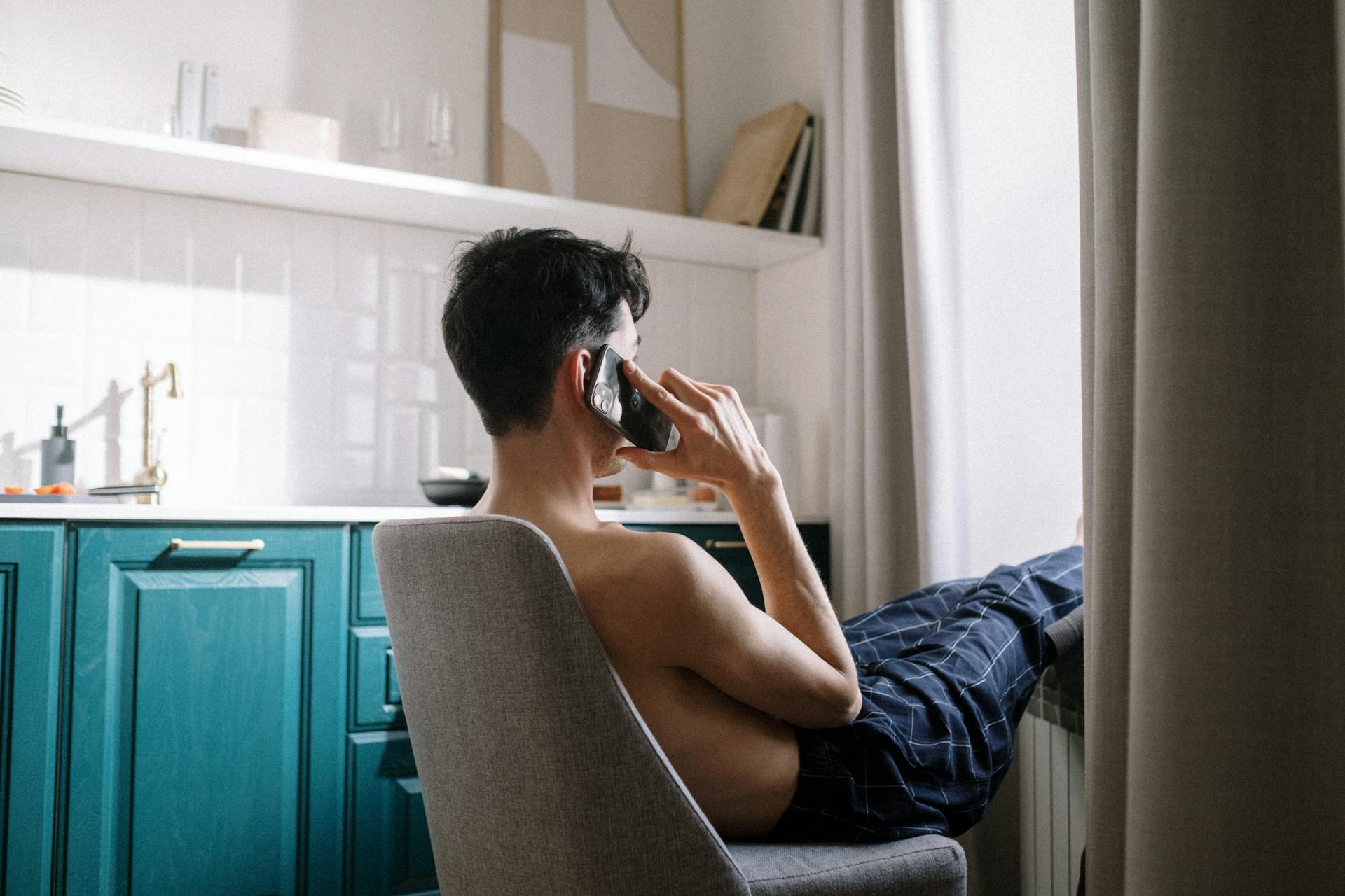 A side-view of a man sitting on a chair and talking on his phone | Source: Pexels