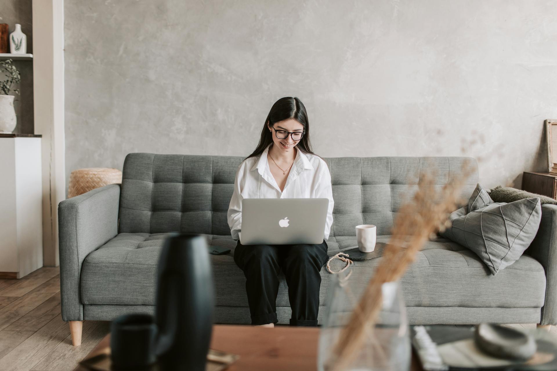 A woman on a couch drinking coffee and using a laptop | Source: Pexels