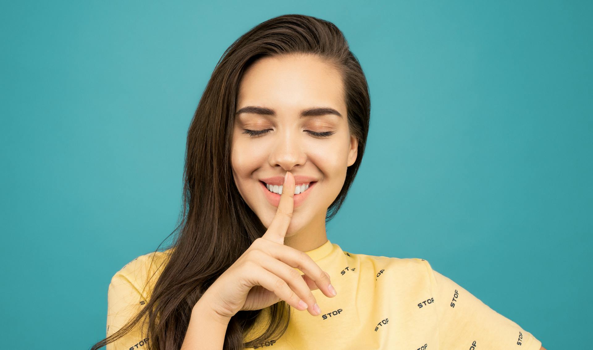 A smiling woman with a finger pressed against her lips | Source: Pexels