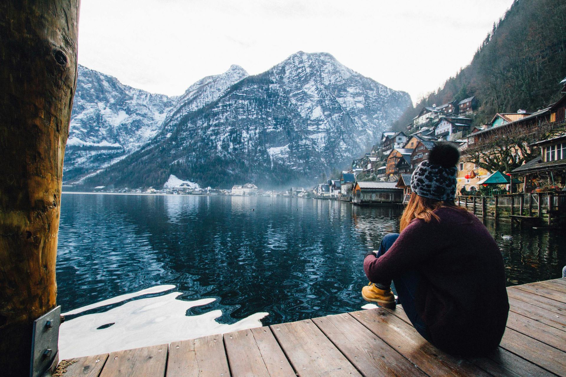A woman sitting on a wooden deck, gazing at the lake and mountains | Source: Pexels