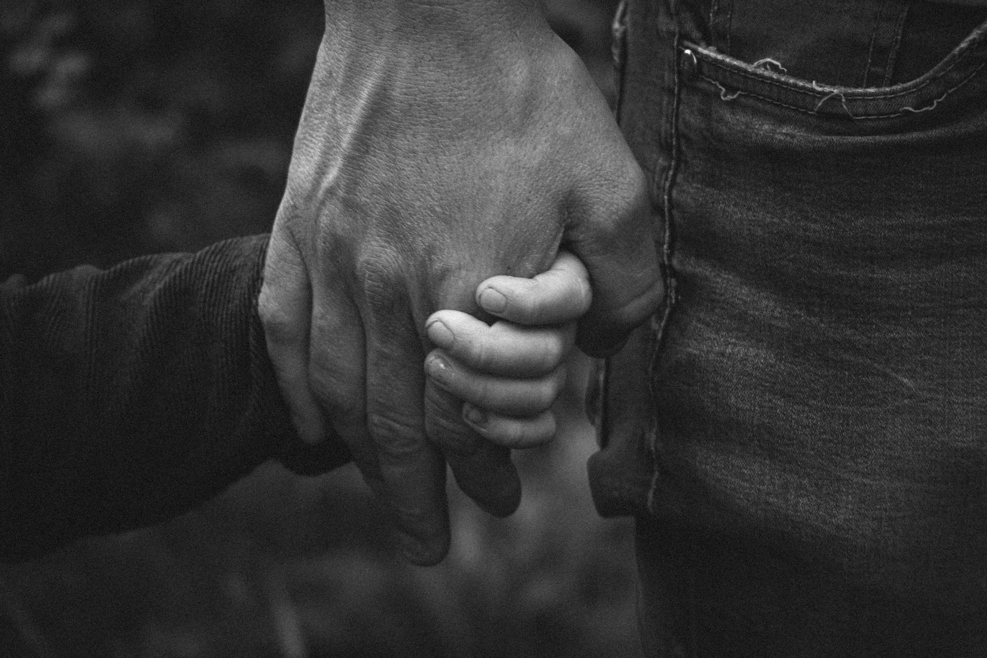 Grayscale shot of a man holding a child's hand | Source: Pexels