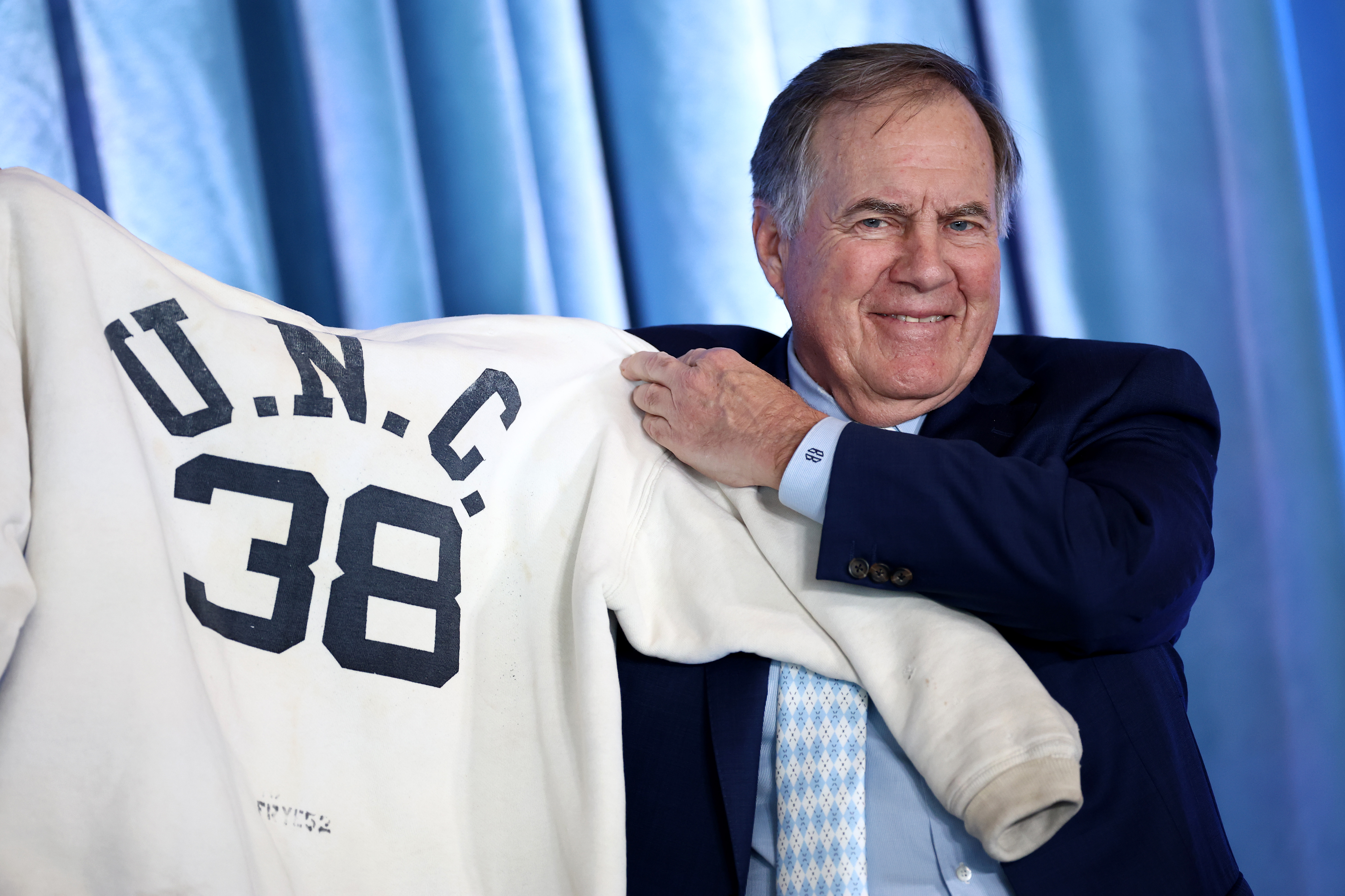 Bill Belichick posing with a UNC football jersey. | Source: Getty Images