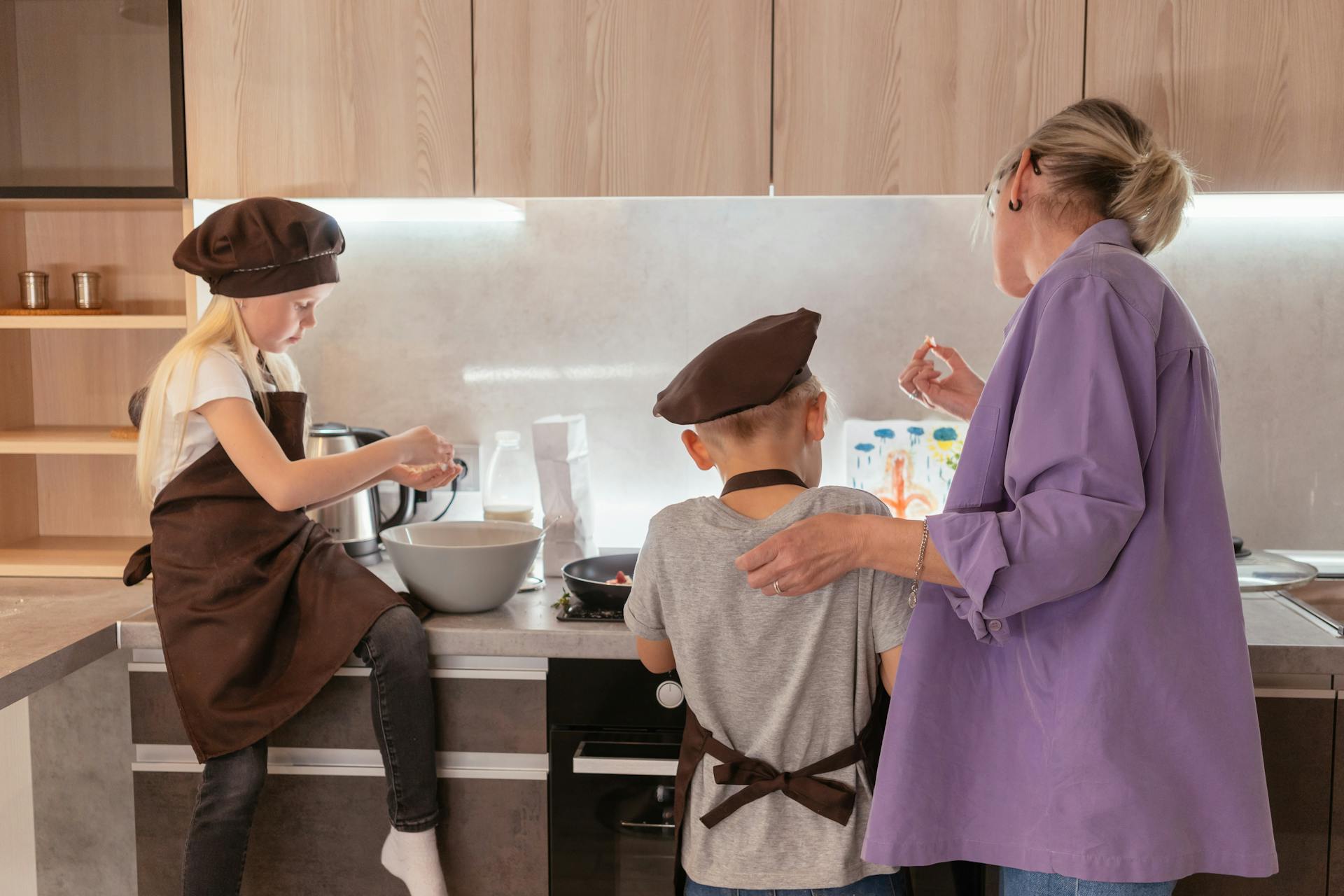 A grandma standing next to her grandkids in the kitchen | Source: Pexels
