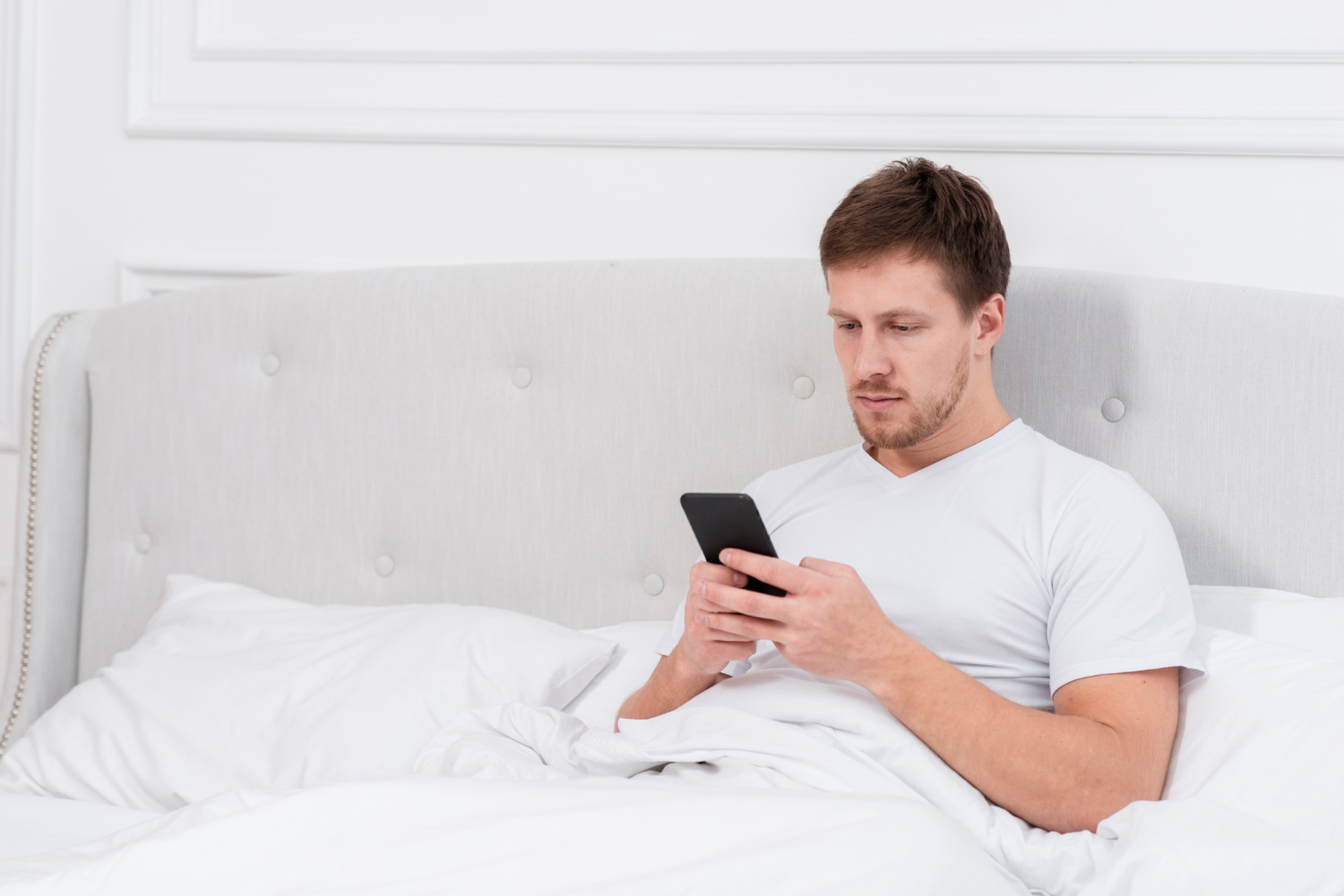 A man sitting on his bed and staring at his phone | Source: Freepik