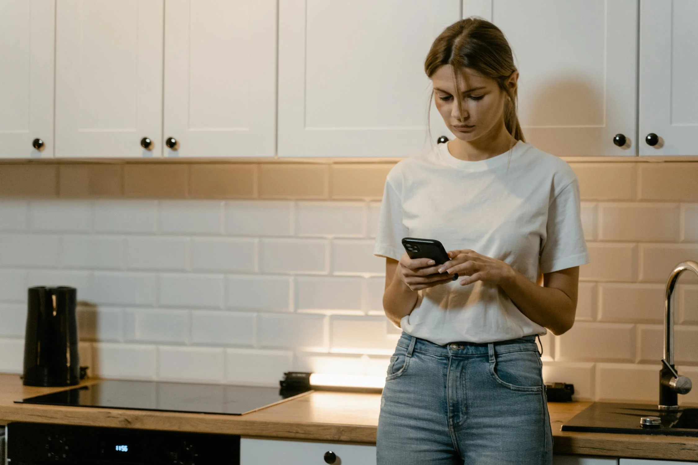 A woman typing on her phone in her kitchen | Source: Pexels