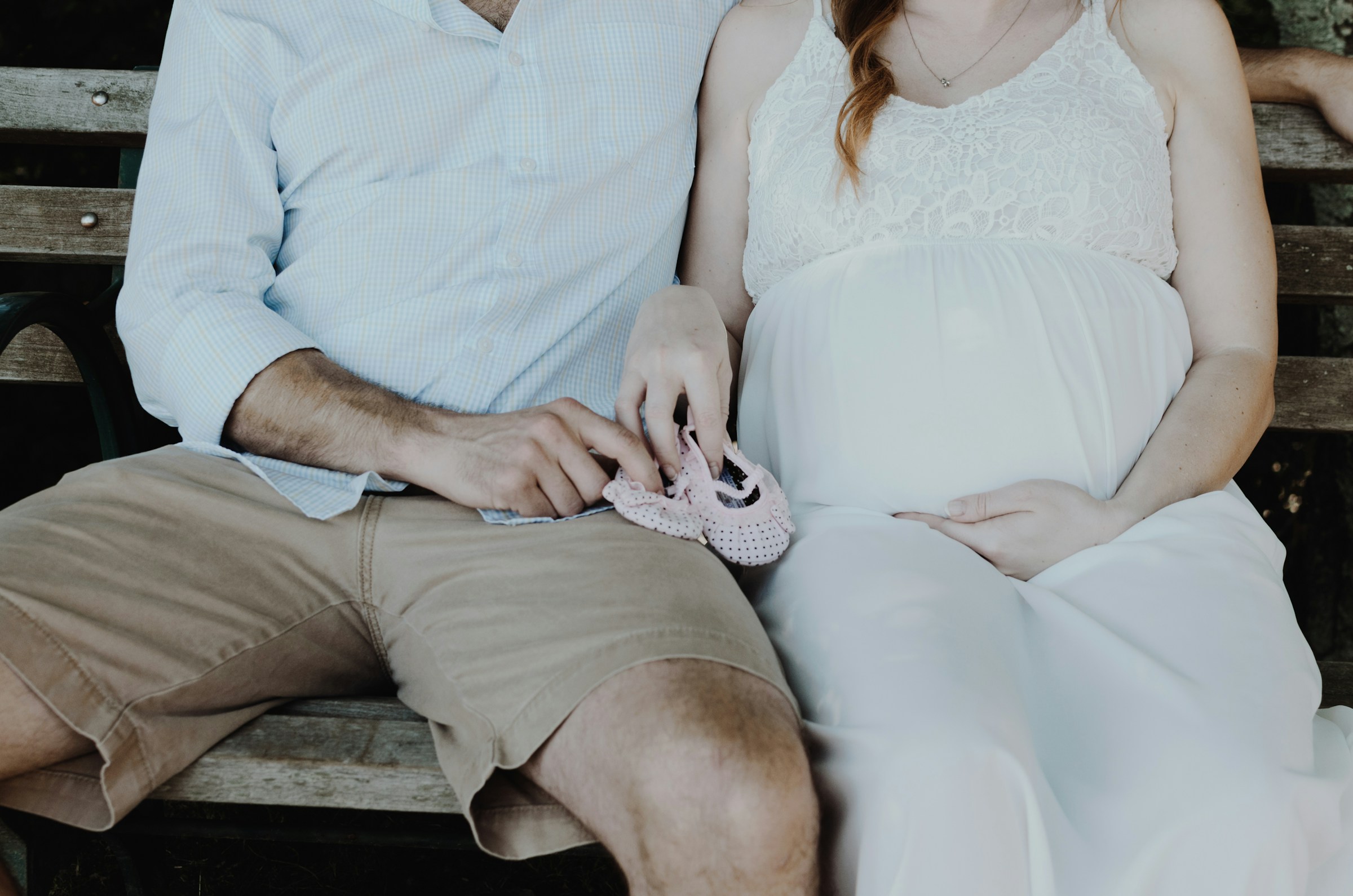 A pregnant couple sitting on a wooden bench | Source: Unsplash