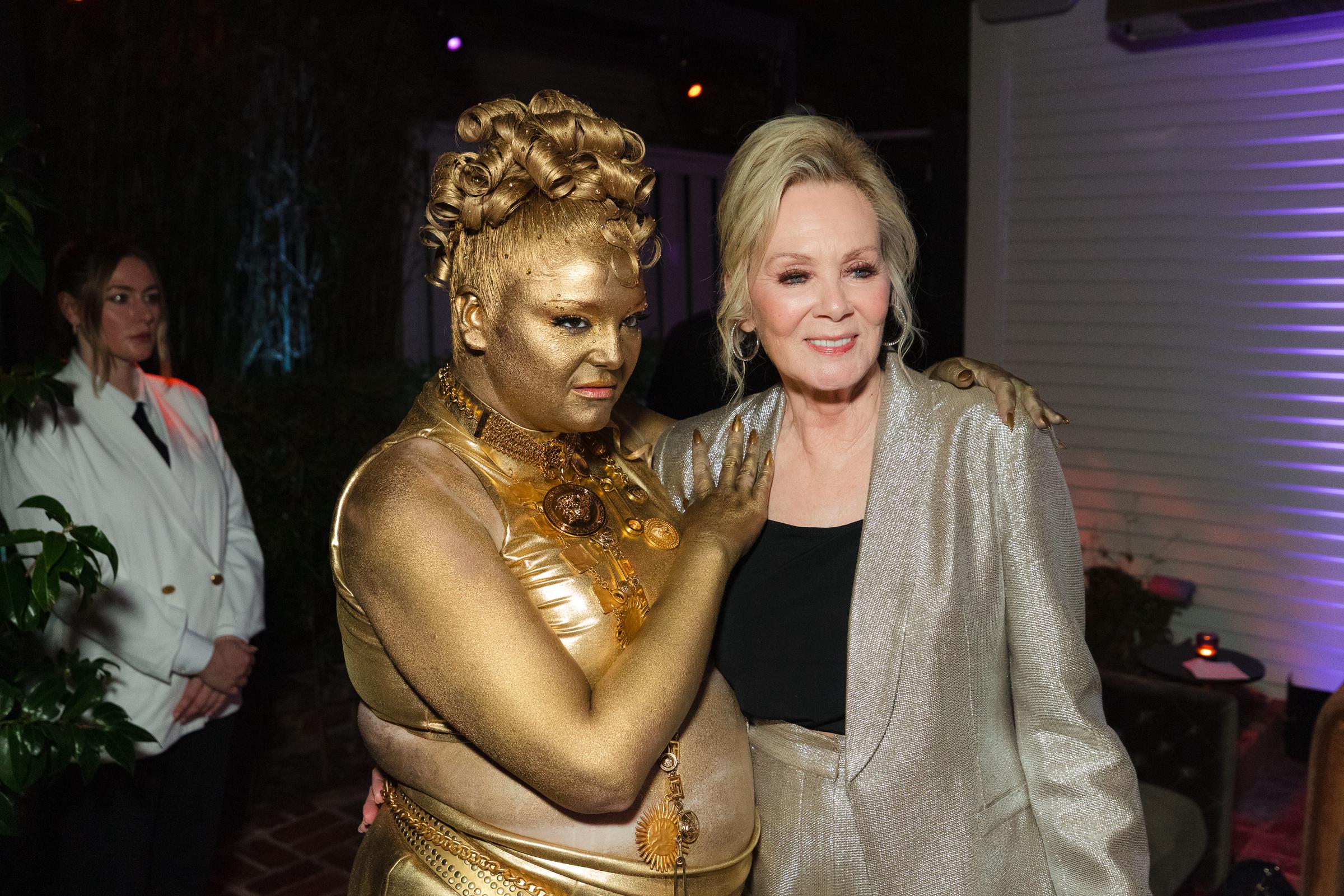 Meg Stalter poses with Jean Smart at the HBO Max afterparty, with Stalter covered in gold body paint and Smart dressed in a shimmering silver jacket. | Source: Getty Images