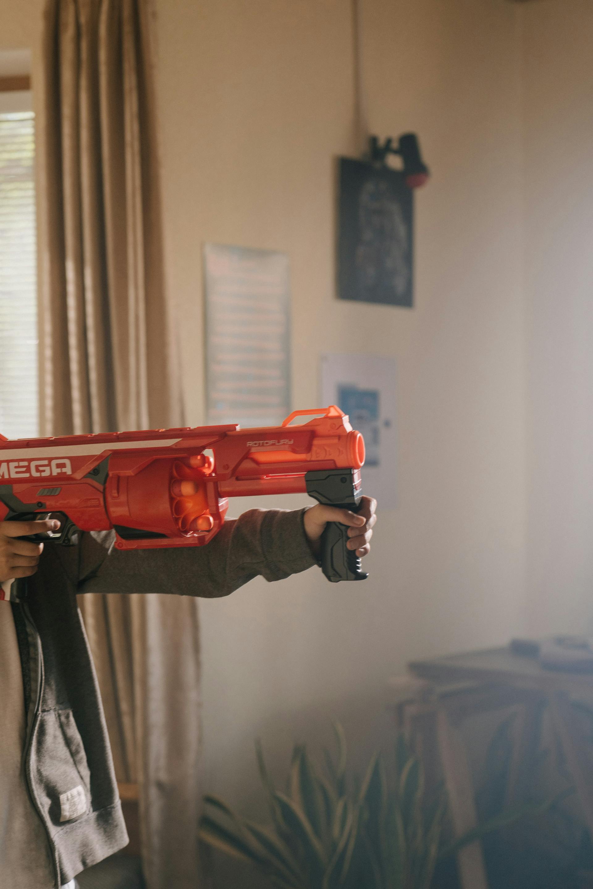 A closeup shot of a young boy holding a red plastic toy gun | Source: Pexels