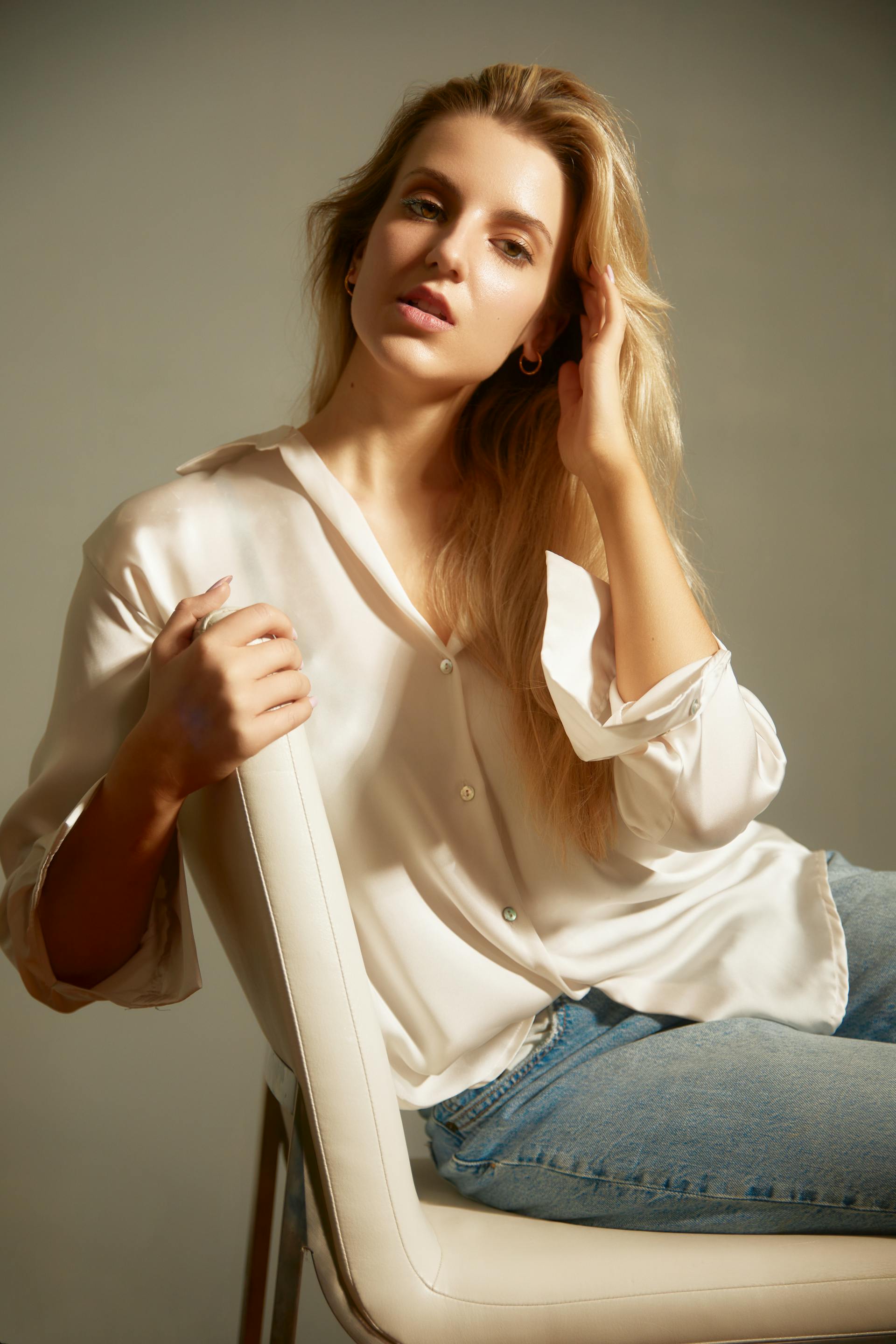 A blonde woman in a white silk shirt and jeans sitting on a white chair | Source: Pexels