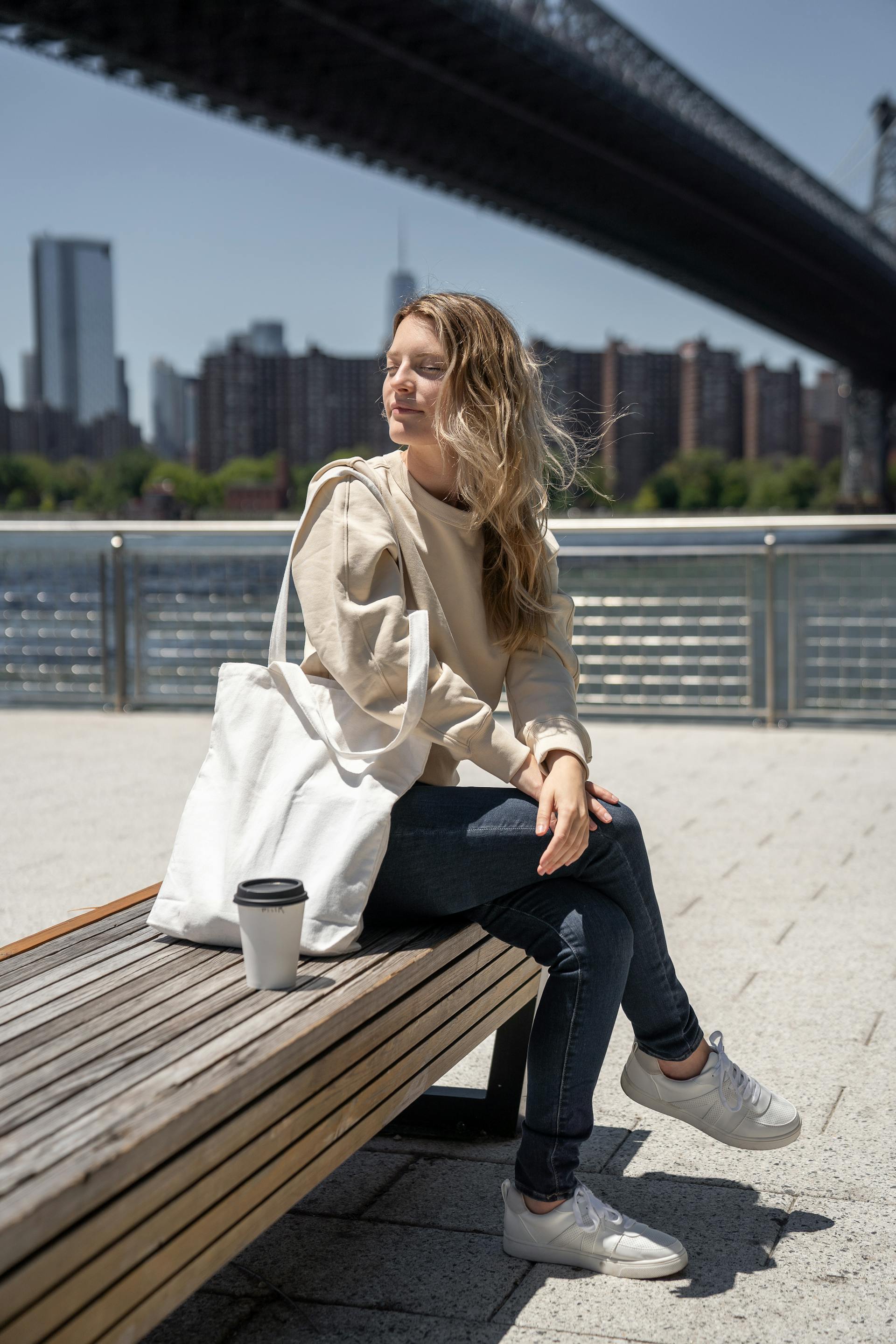 A woman sitting on a bench with her white bag and a coffee | Source: Pexels