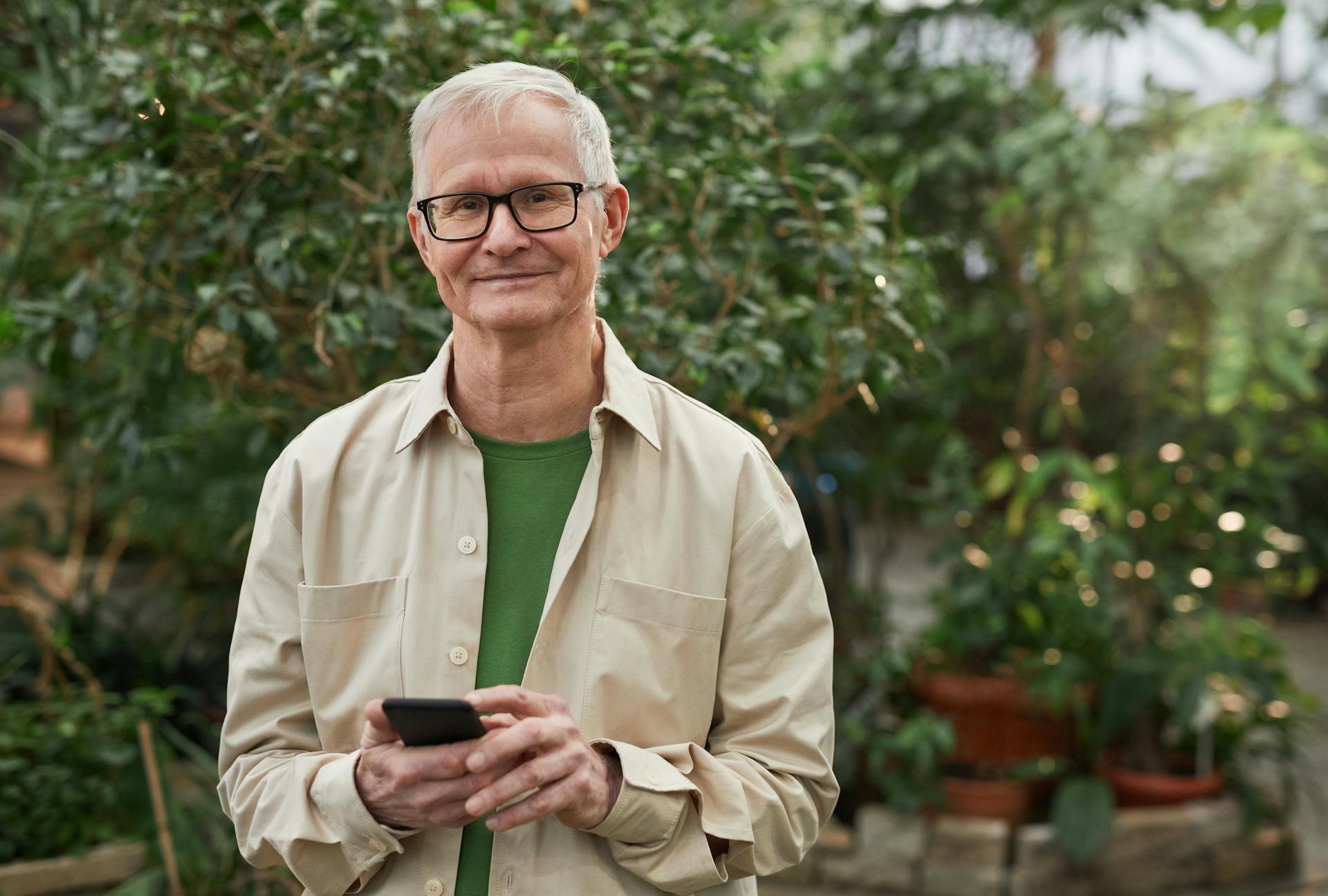 A happy mature man in glasses and a button-up shirt holding a phone | Source: Pexels