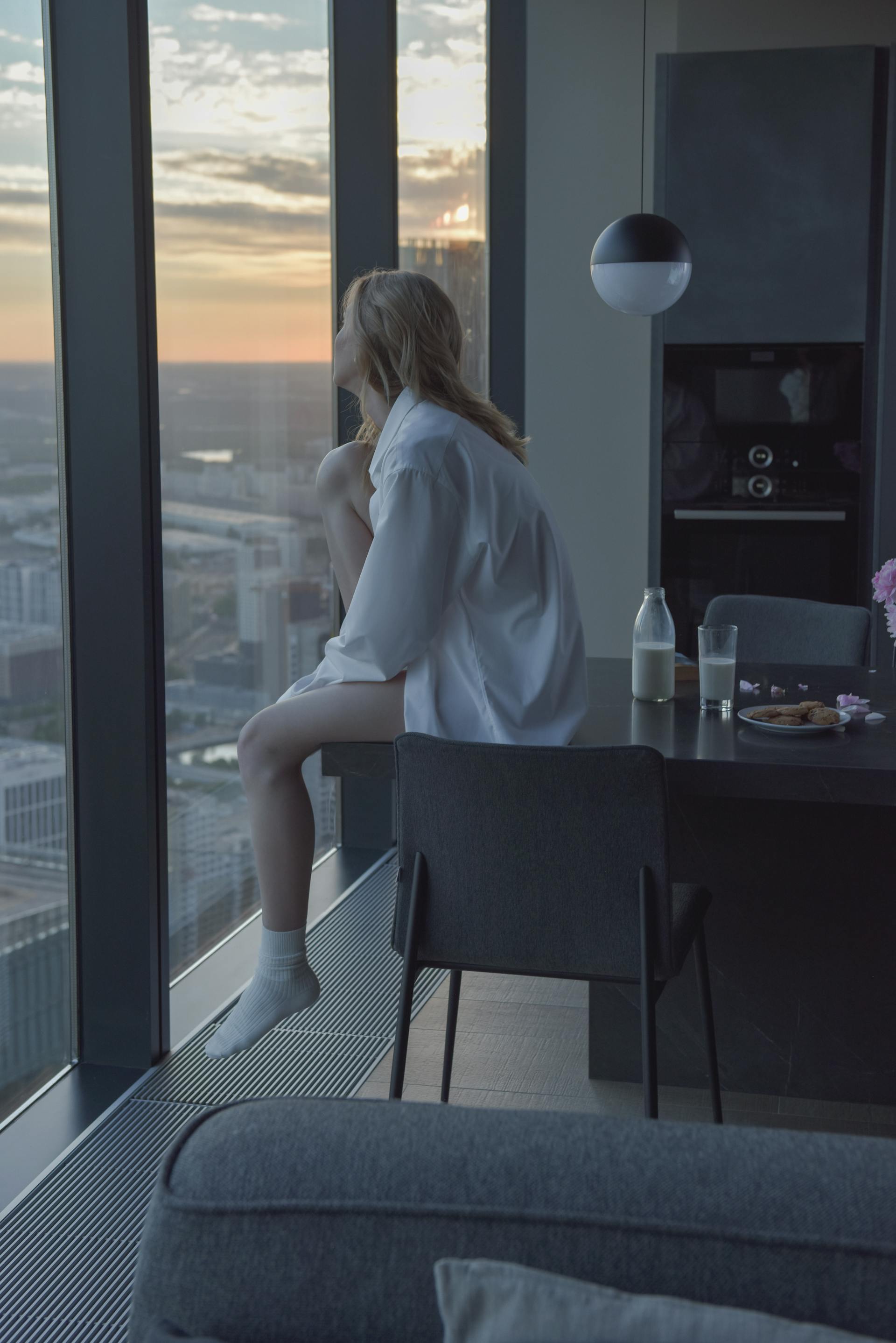 A woman in a white shirt sitting on a table and looking out the window | Source: Pexels