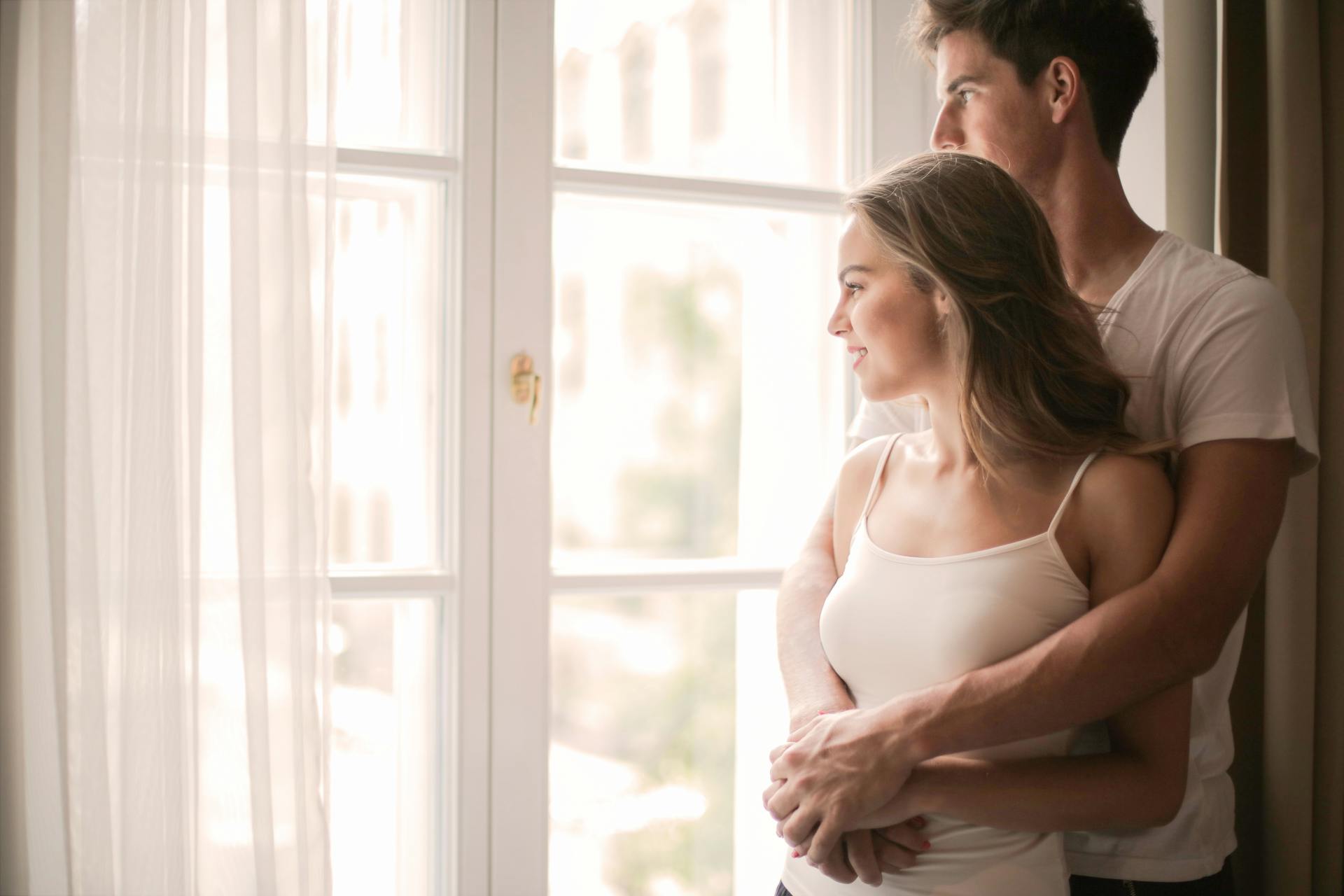 A couple cuddling while standing near the window in a room | Source: Pexels