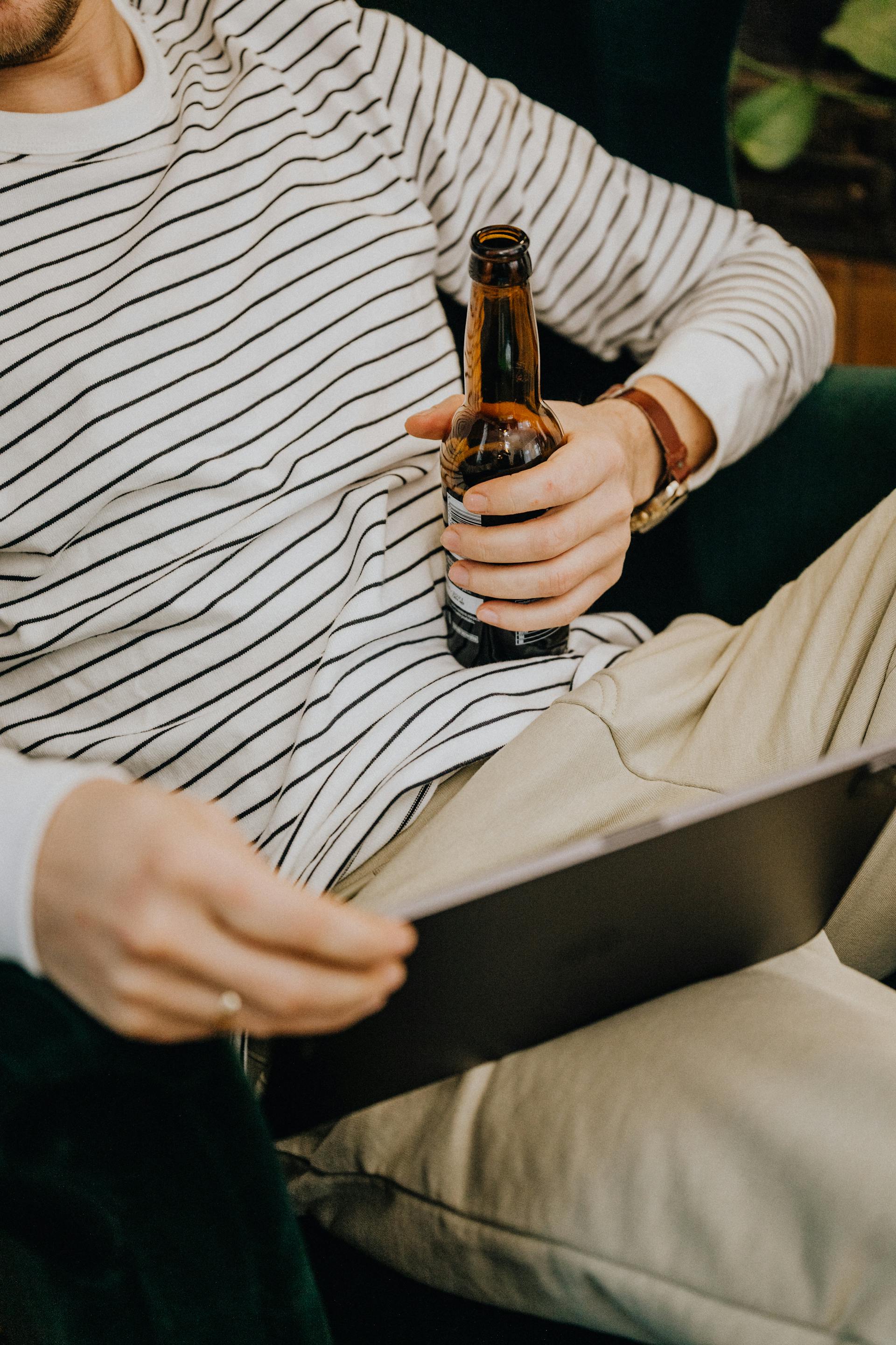 A close-up shot of a man holding a bottle of beer and looking at his tablet | Source: Pexels