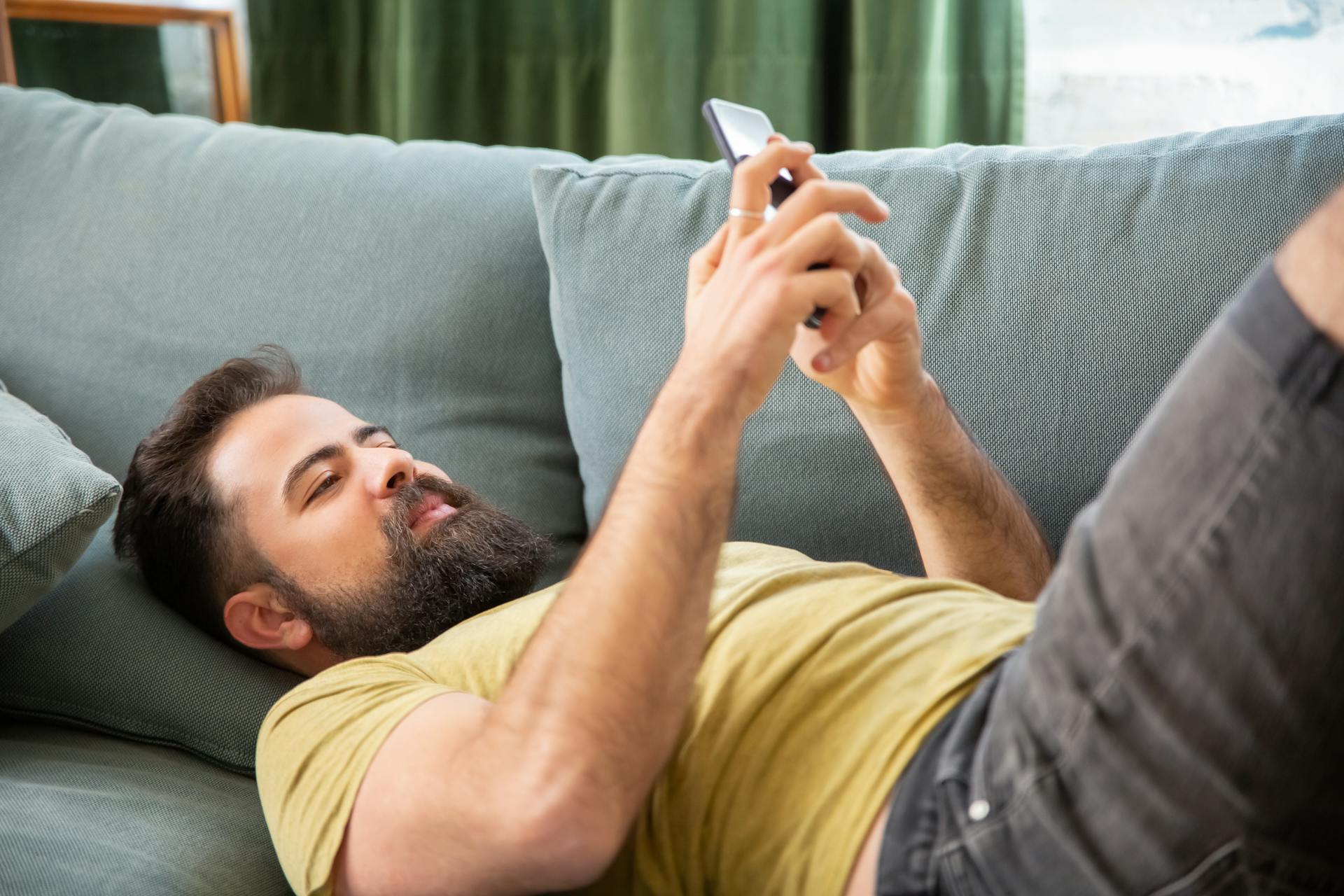 A man using his phone while lying on the sofa | Source: Pexels