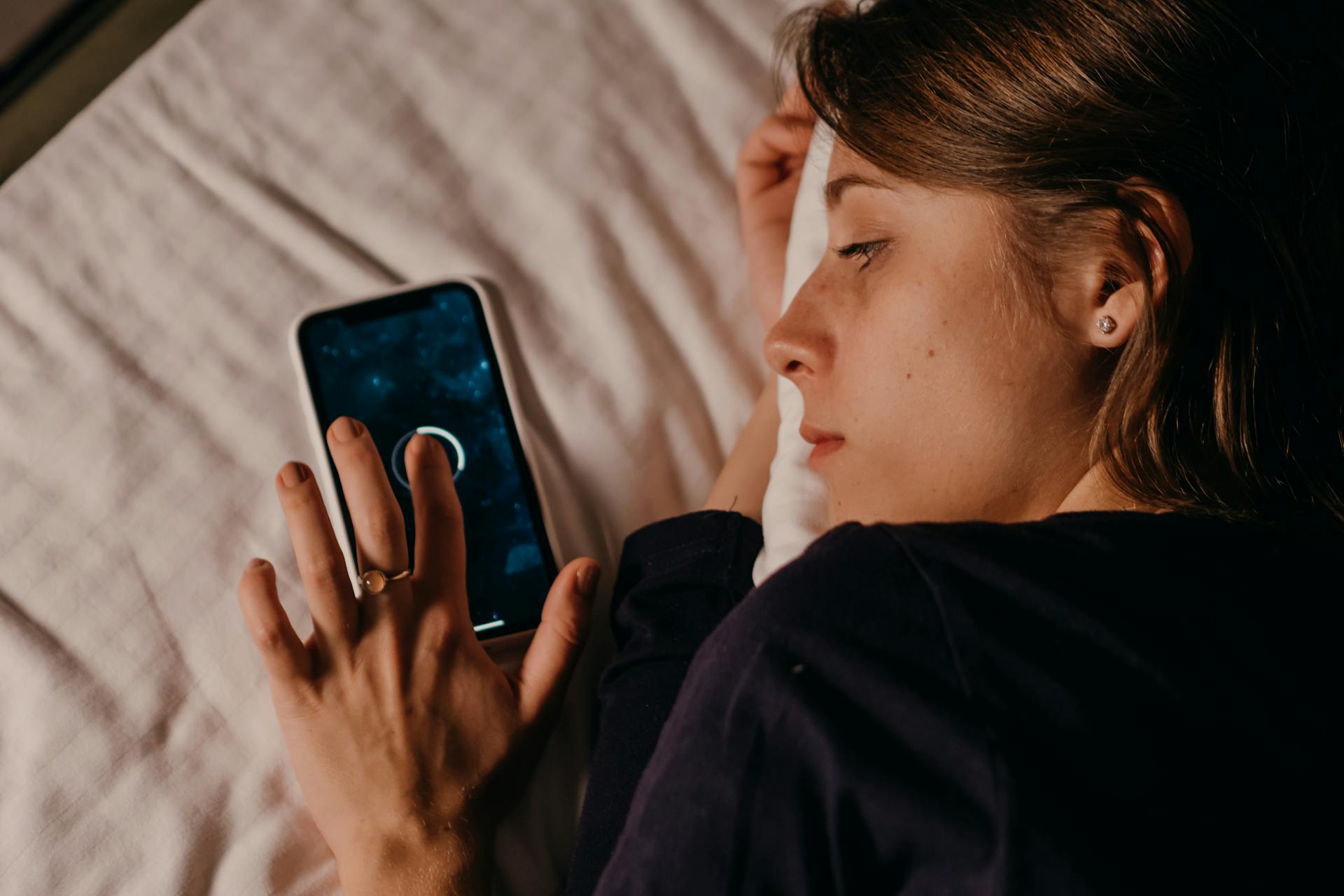 Woman lying on a bed while using her smartphone | Source: Pexels