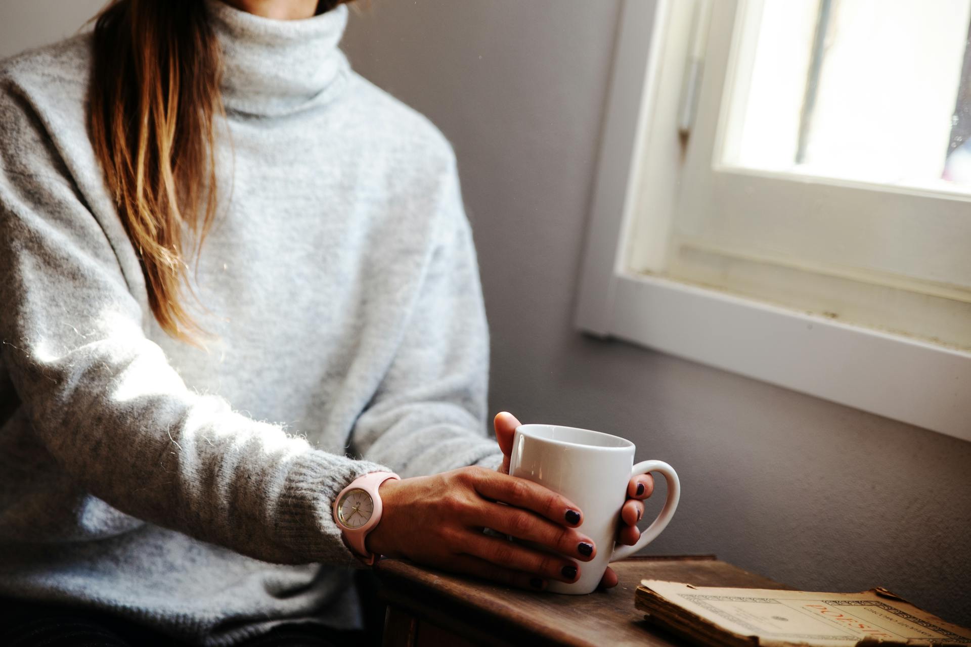A woman holding a coffee mug and sitting beside the window | Source: Pexels