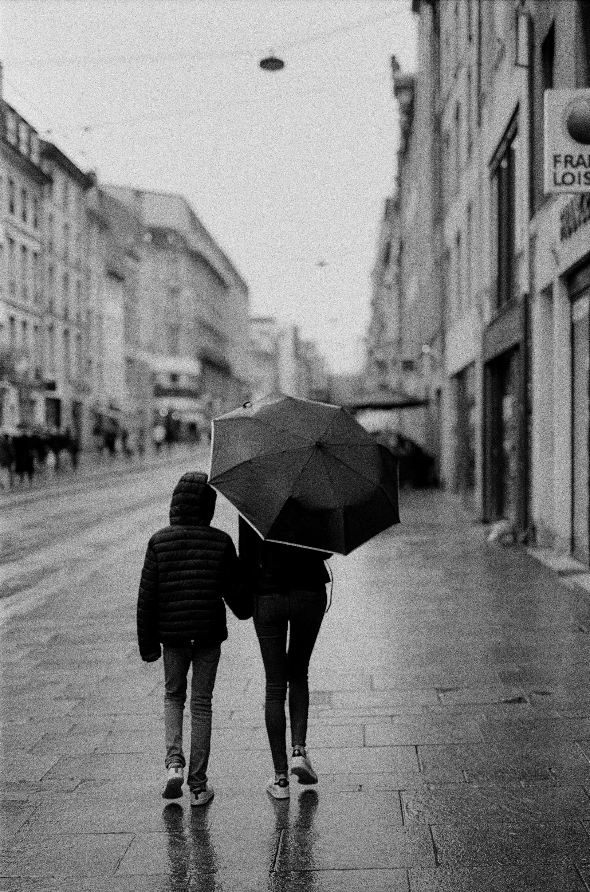 Grayscale shot of a woman walking with a boy on a rainy day | Source: Pexels