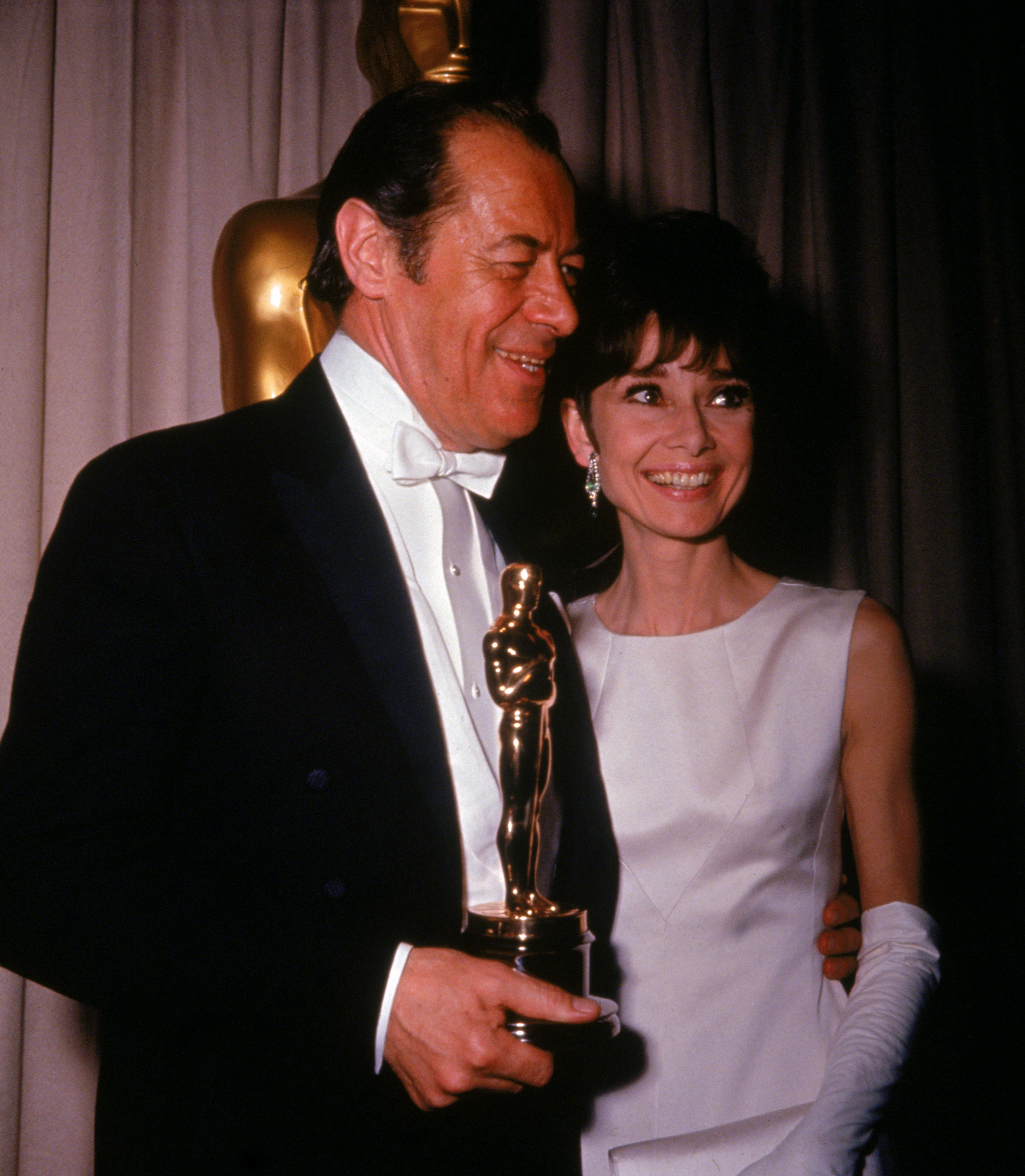 Rex Harrisonholds his Best Actor Oscar for the film, “My Fair Lady,” while standing with his costar, actor Audrey Hepburn during the Academy Award ceremonies, Santa Monica, California, April 5, 1965. | Source: Getty Images