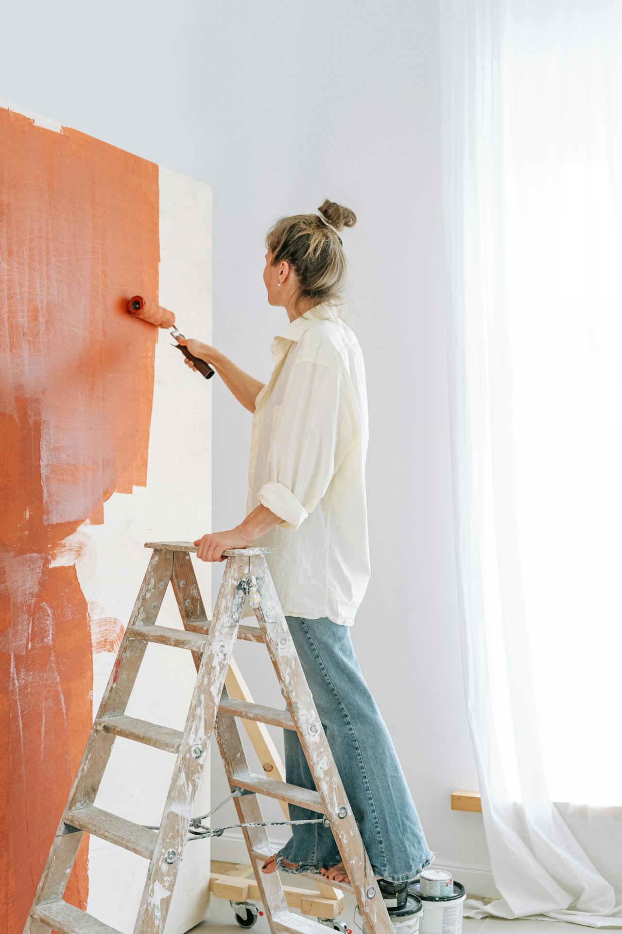A woman standing on a ladder and painting a wall | Source: Pexels