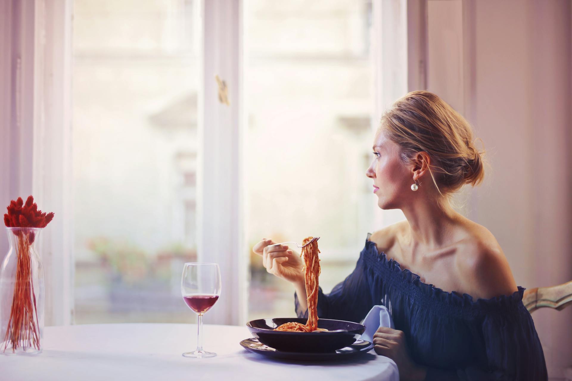 An elegant woman seated at a table and enjoying a pasta dish | Source: Pexels
