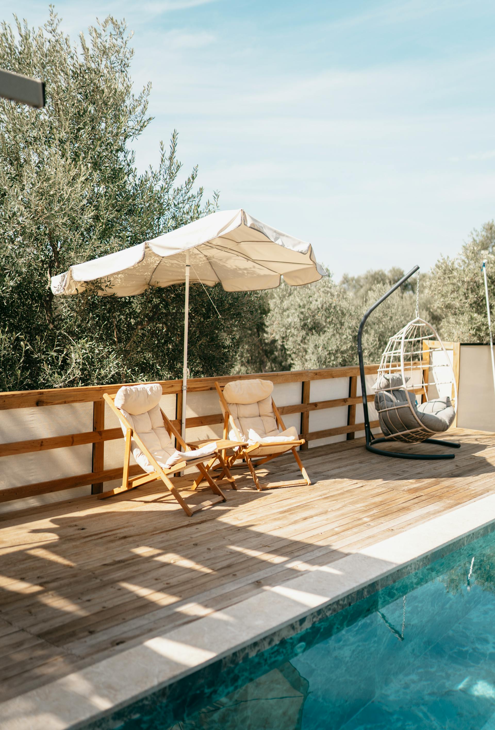 An umbrella and deck chairs placed near a pool | Source: Pexels